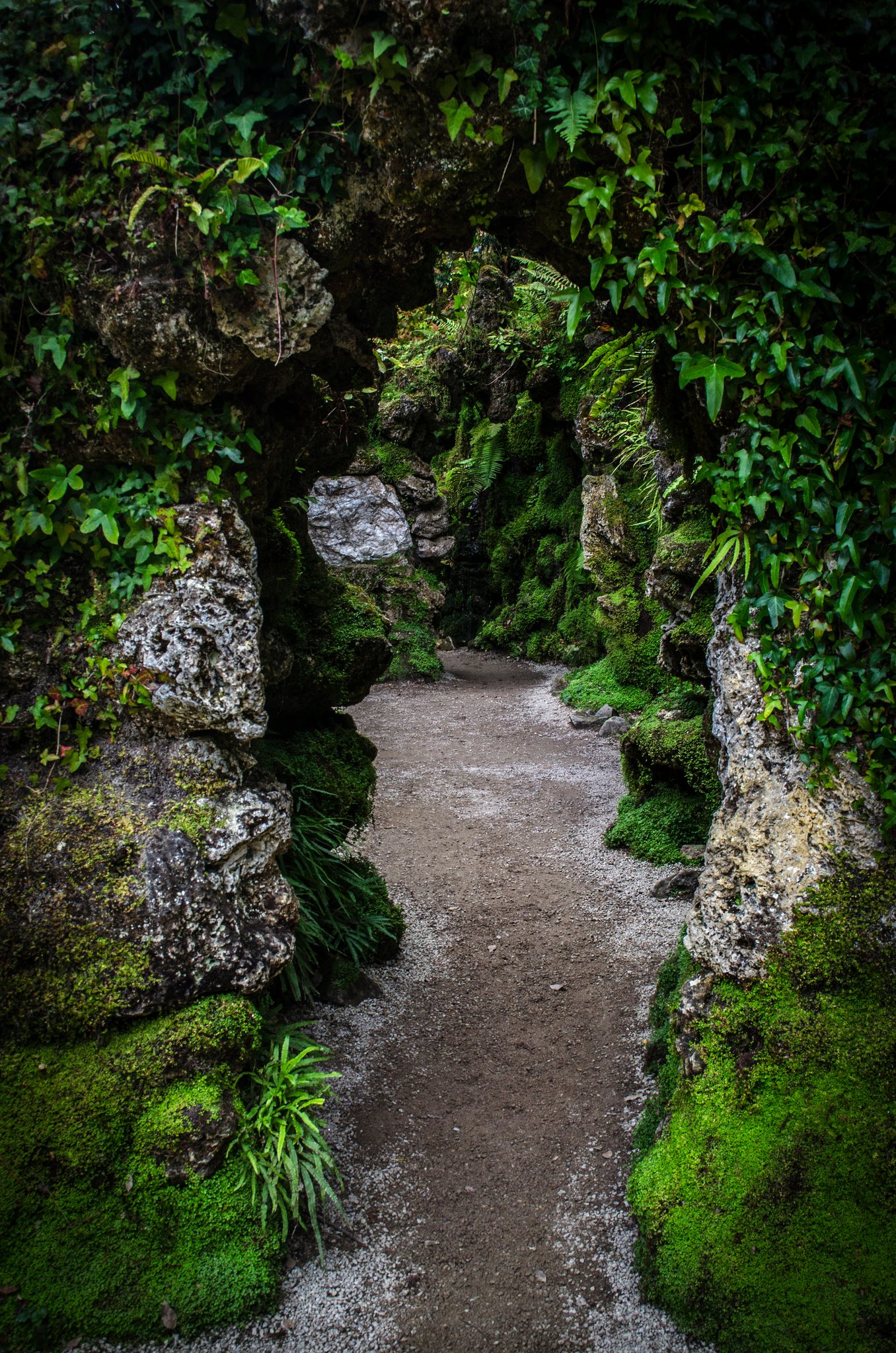 A path winds through a mossy stone passage into the green.