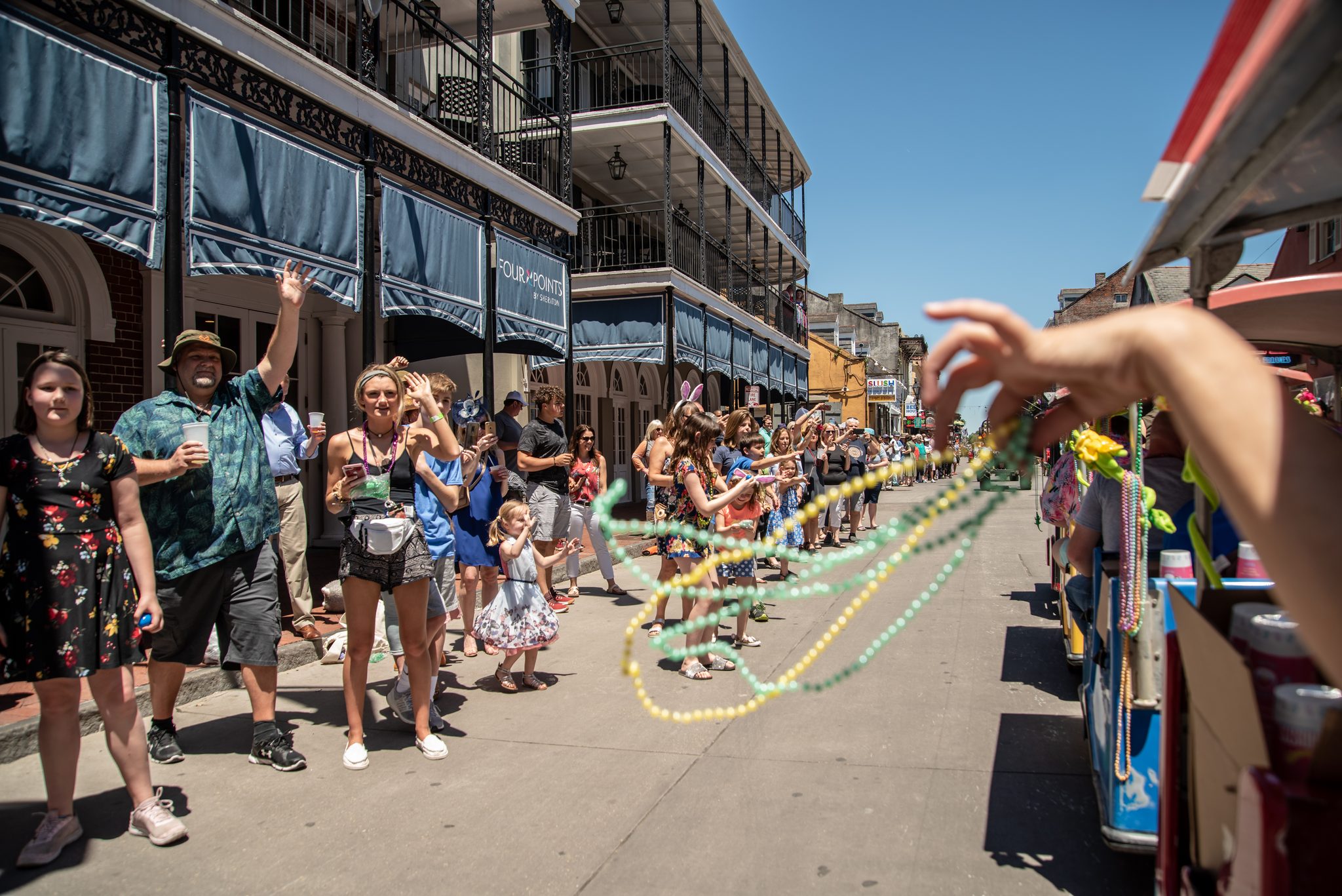 Beads fly from a float into a street full of raised hands.