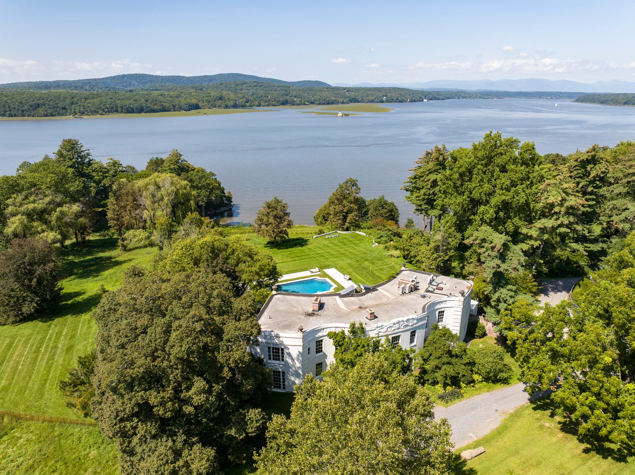 From above in early September, a white villa sits among old trees with the Hudson opening wide beyond the lawns.