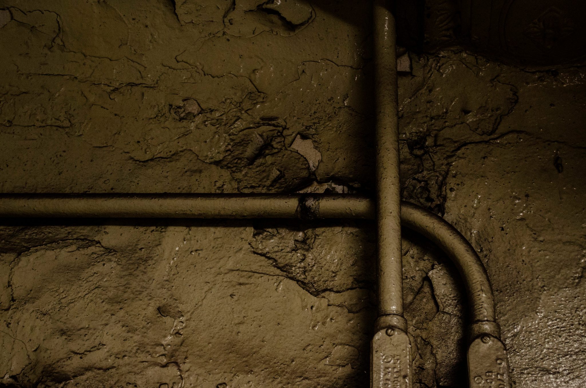 A pipe bends across a wall of cracked and peeling plaster.