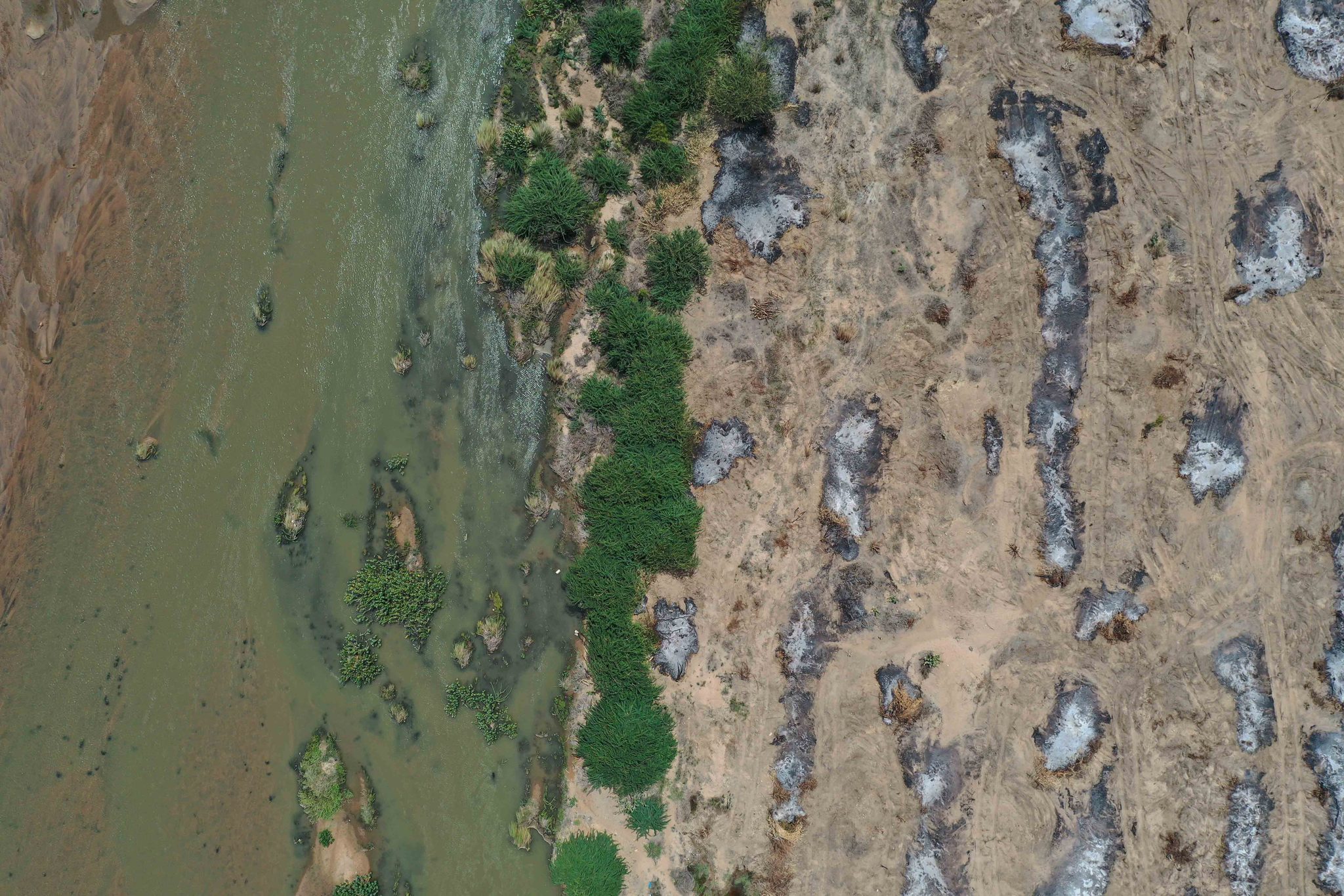 Straight down, green water meets a riverbank pocked with pits.