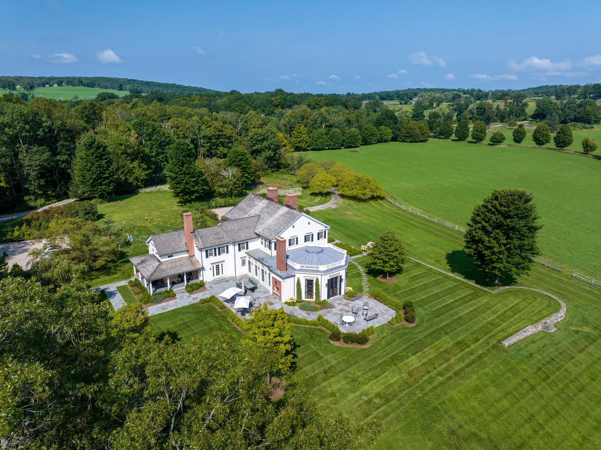 An August morning over a white country house, its lawns mown in stripes and fields running out to the tree line.
