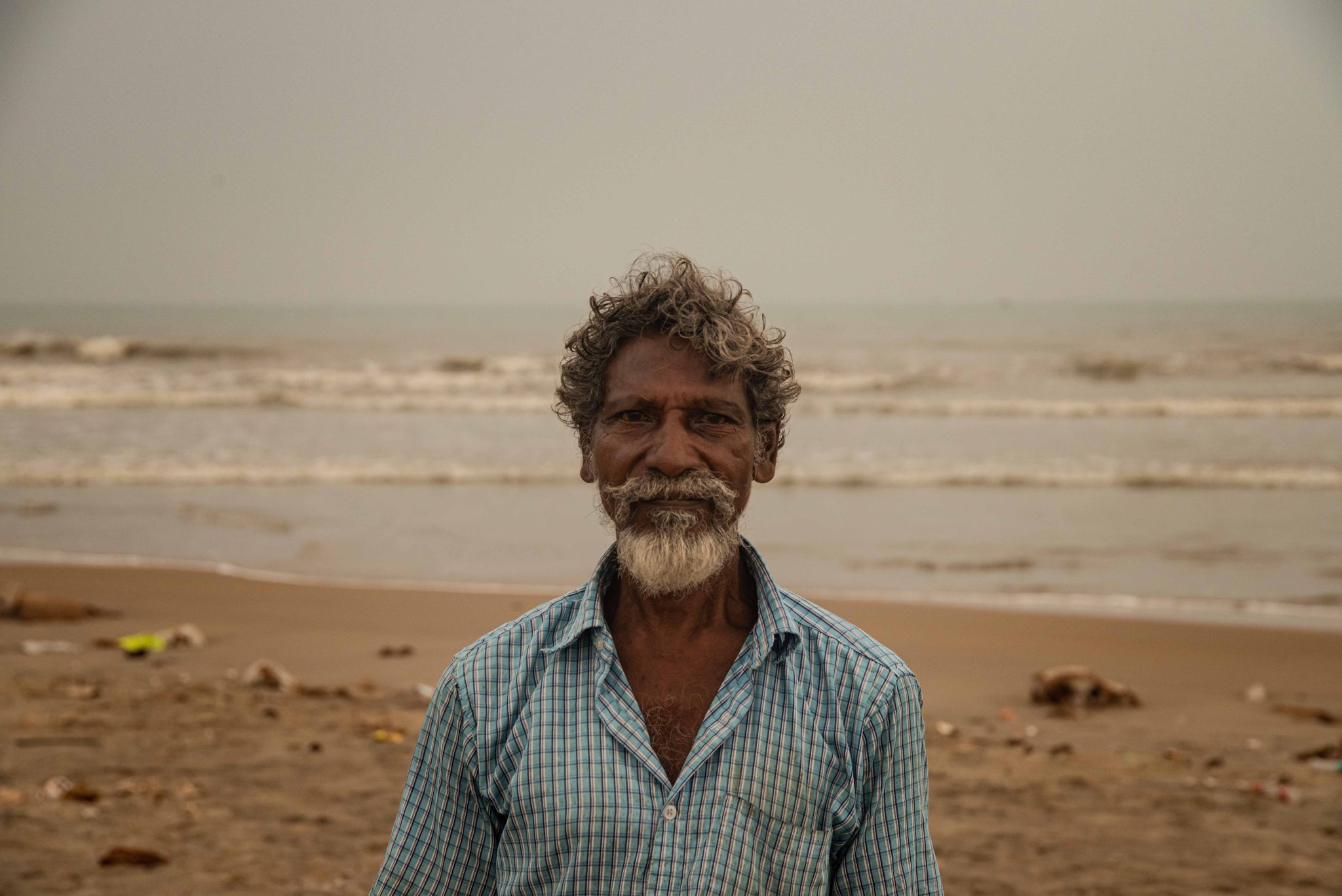 He meets the lens with a small smile, the sea gray behind him.
