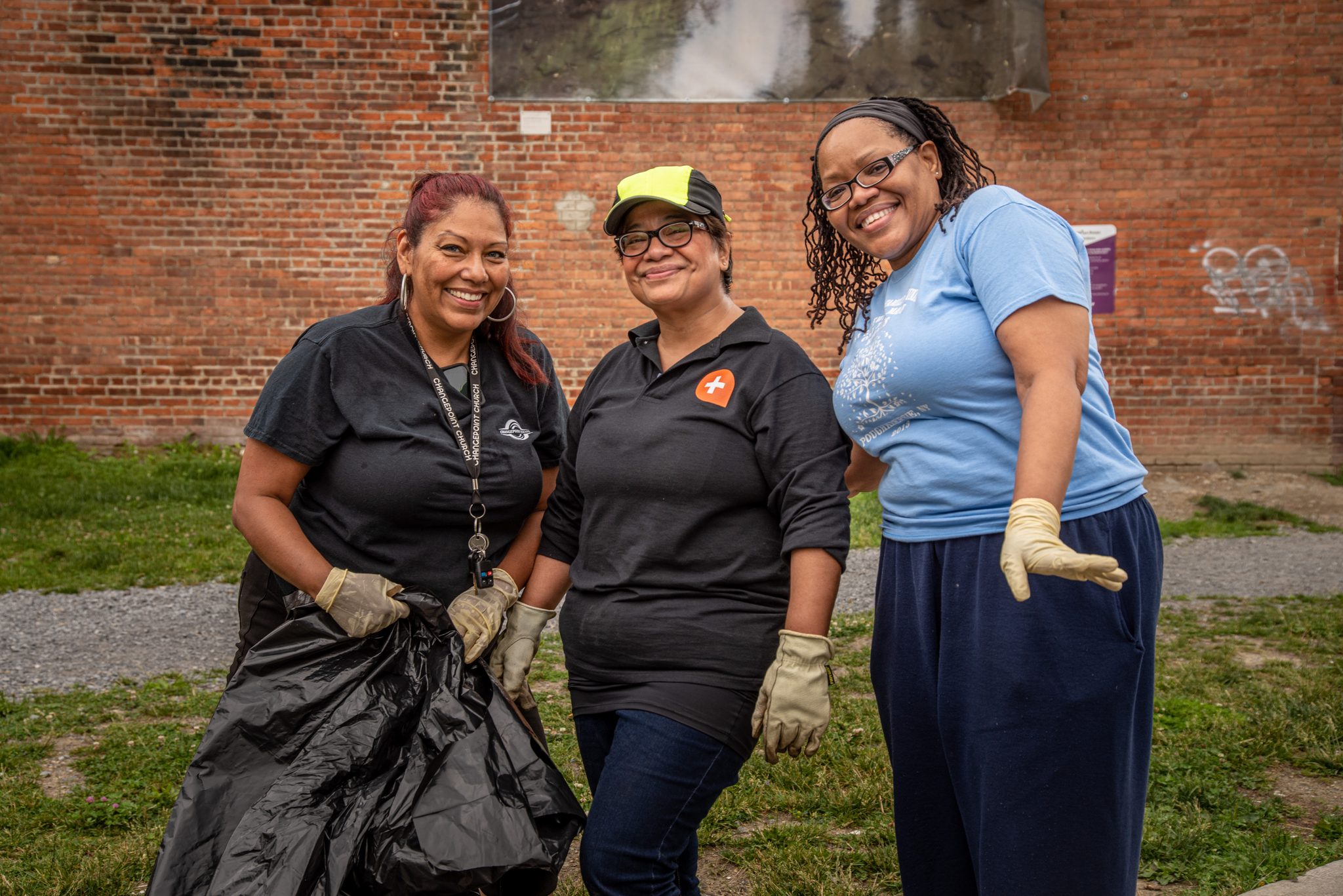Three volunteers in work gloves pose with the bag they've been filling.