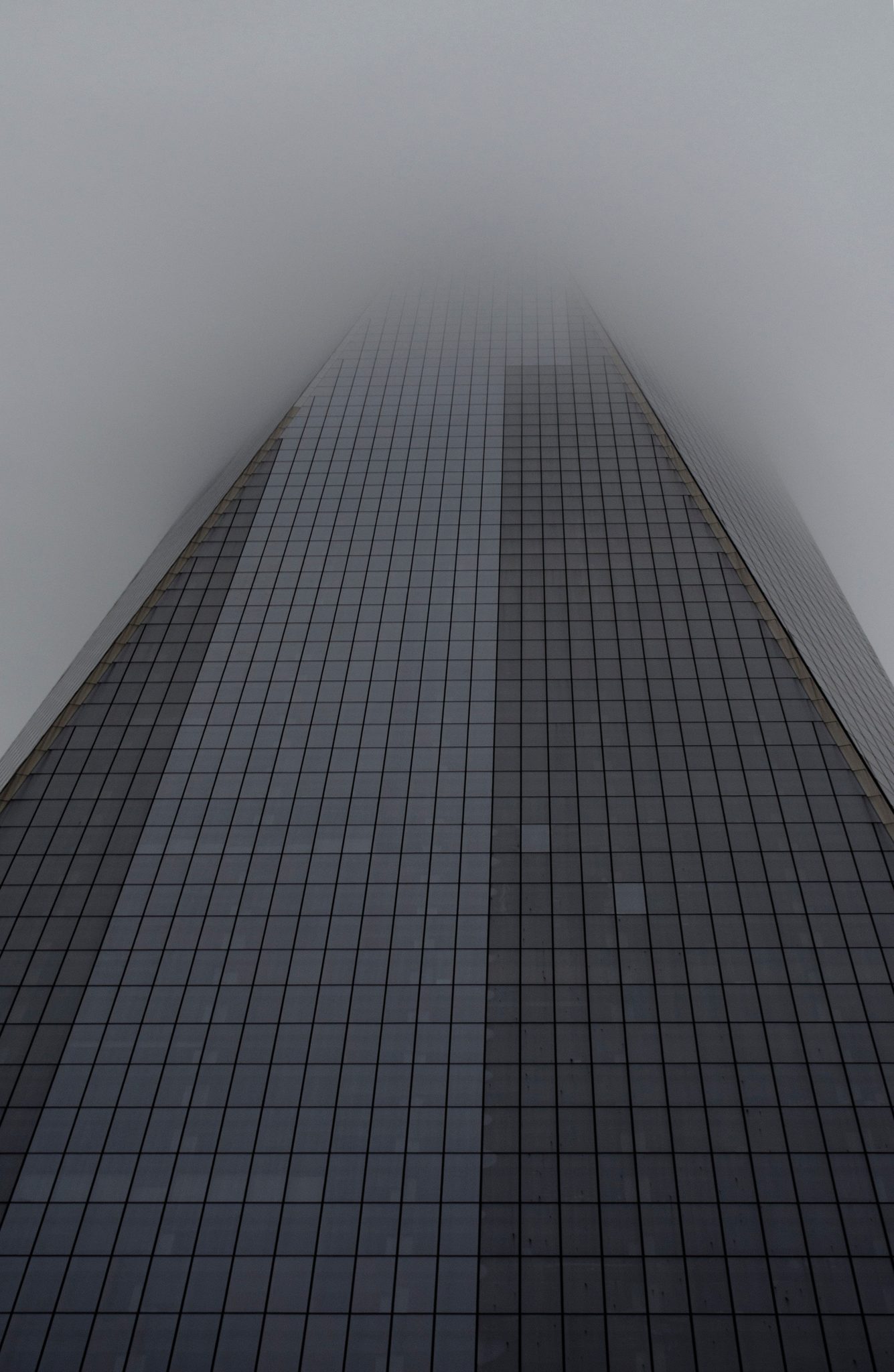 A glass tower vanishes into the fog halfway up.