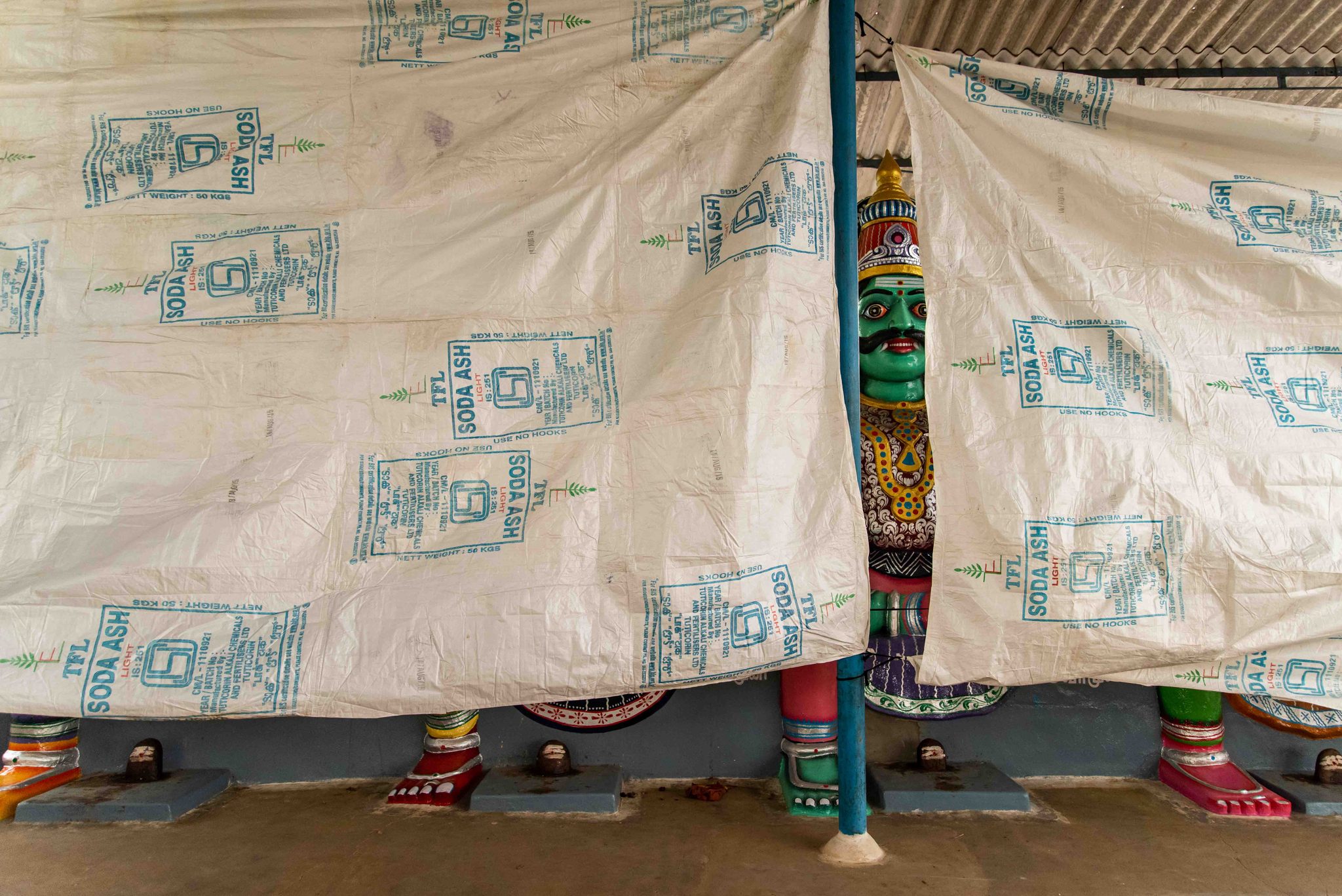 A green-faced deity peeks out from behind a patterned tarp.