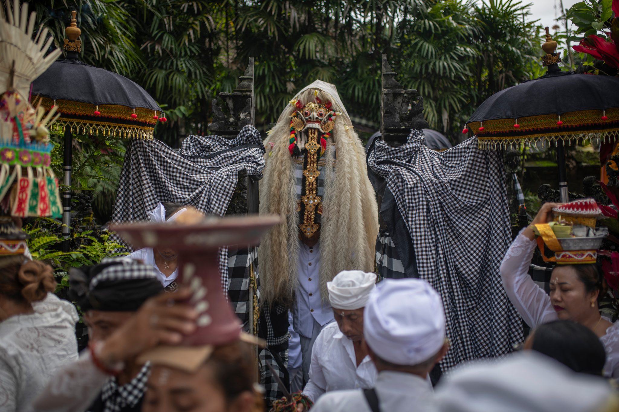 Between shrines draped in checked cloth, the figure waits while offerings pass overhead.