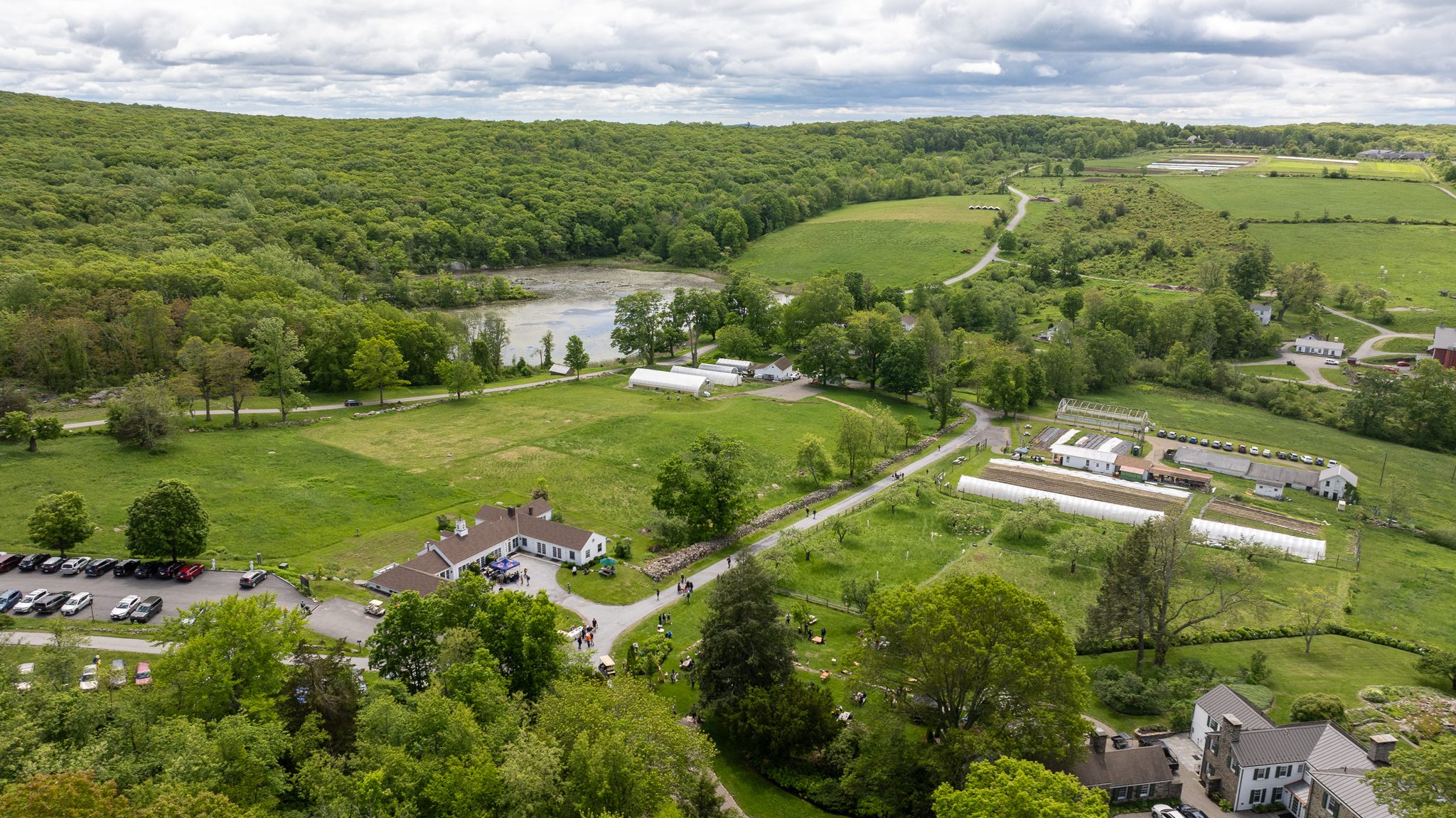 The whole valley in one view: fields, greenhouses, the lake and the wooded ridges around them.