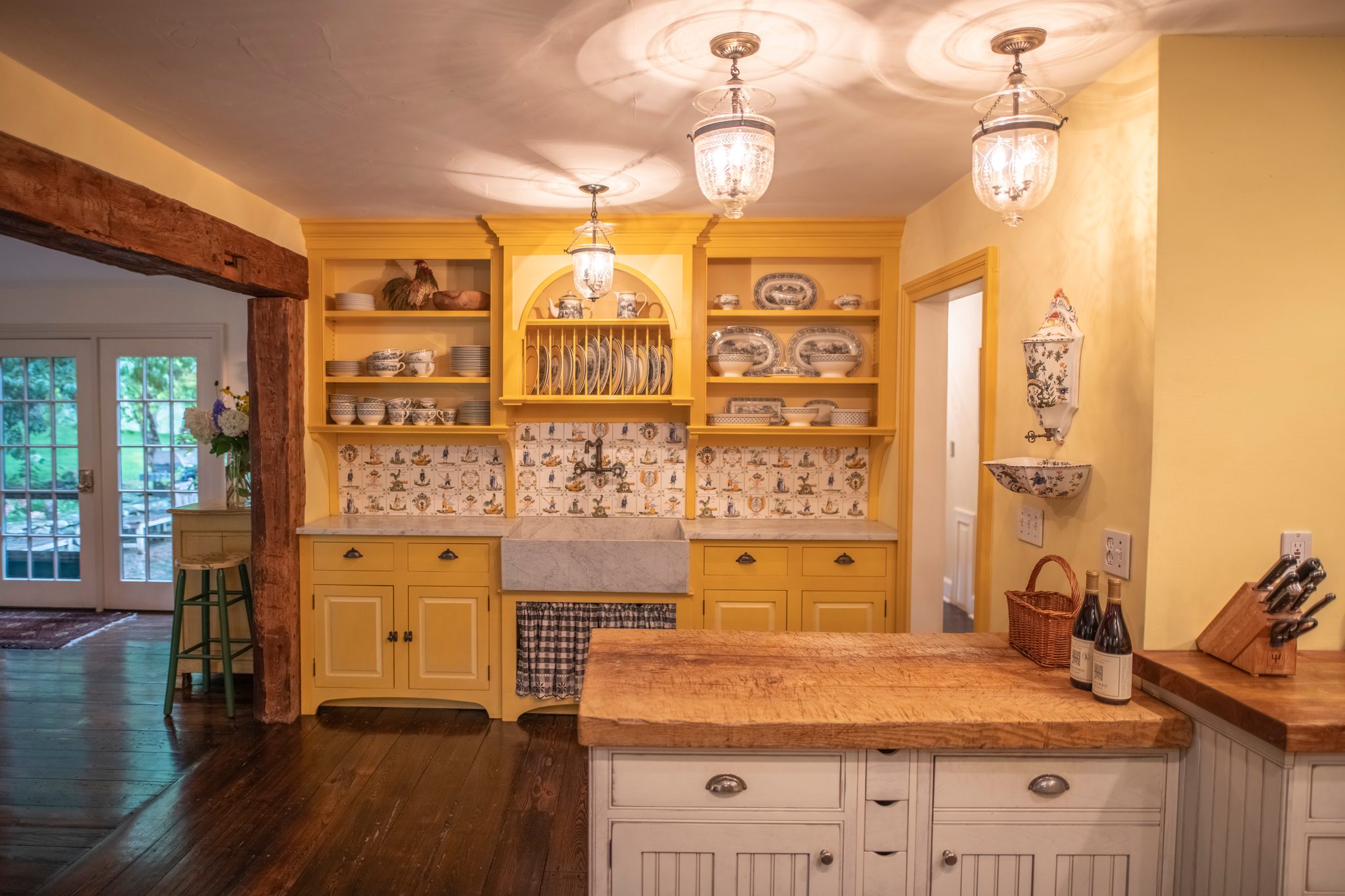 Yellow plate racks, hand-painted tiles and a marble farm sink hold the soft September light in a working country kitchen.