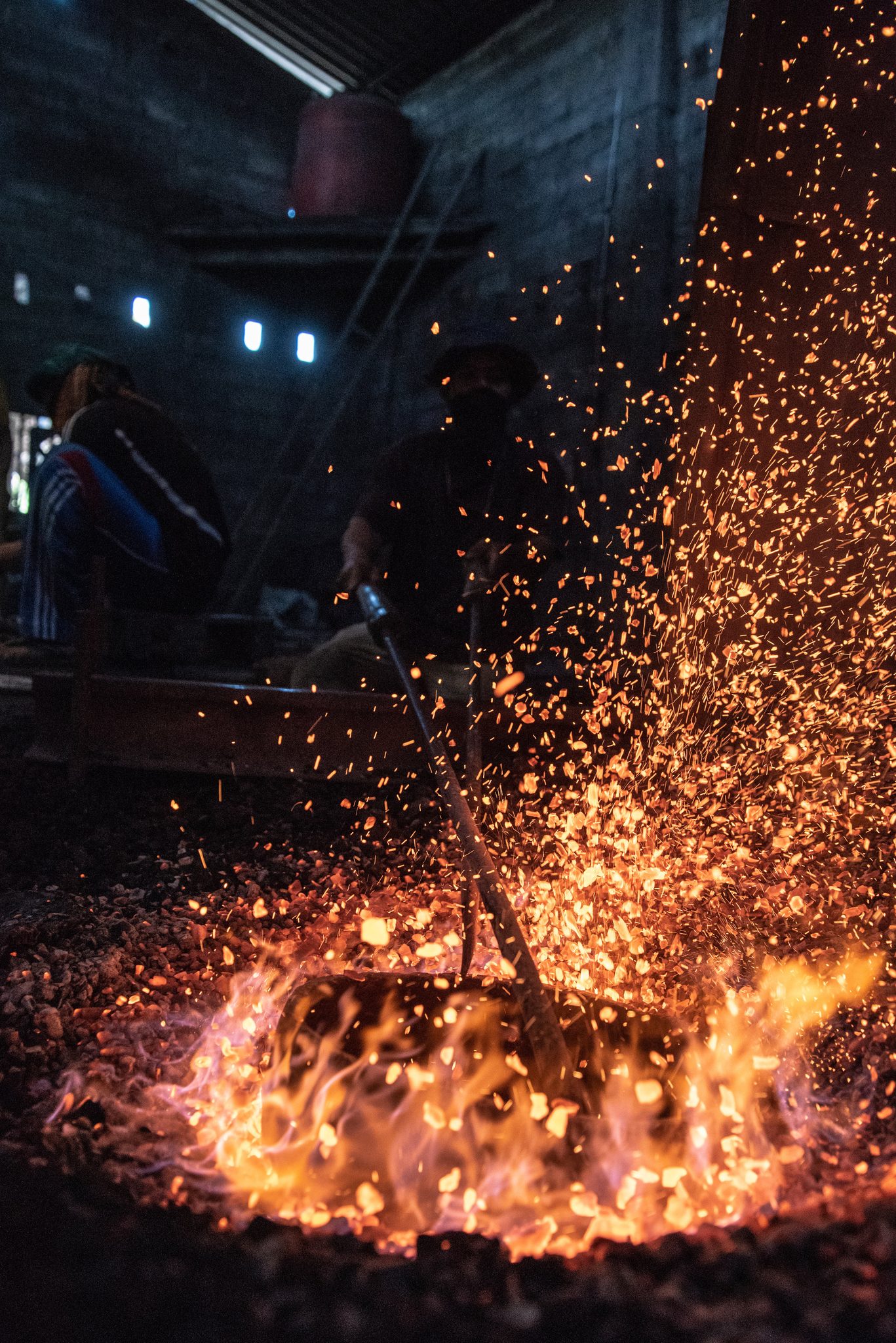Sparks pour upward from the coal pit, a shower of gold in the dark workshop.