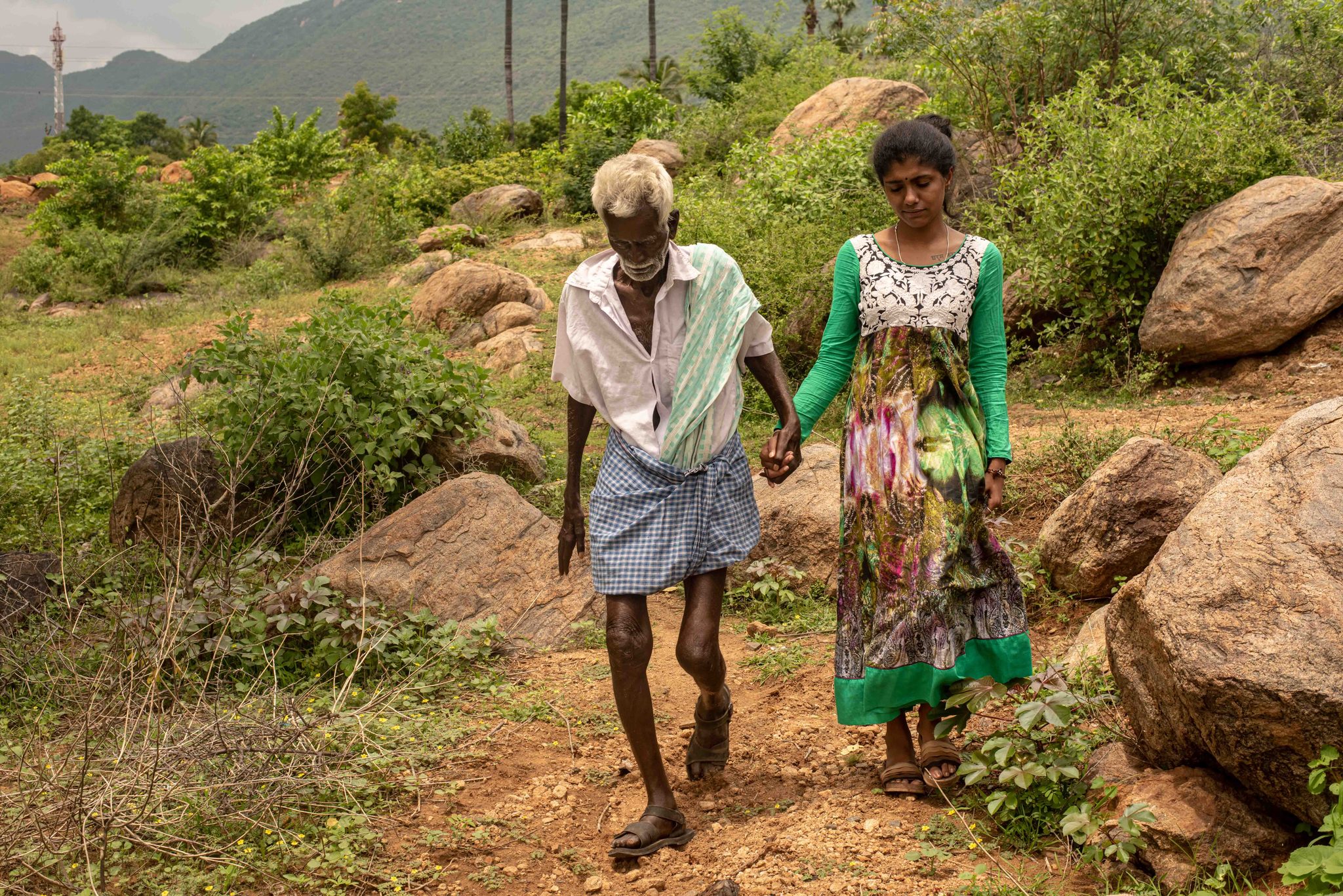 The elder walks hand in hand with a young woman along a rocky path.
