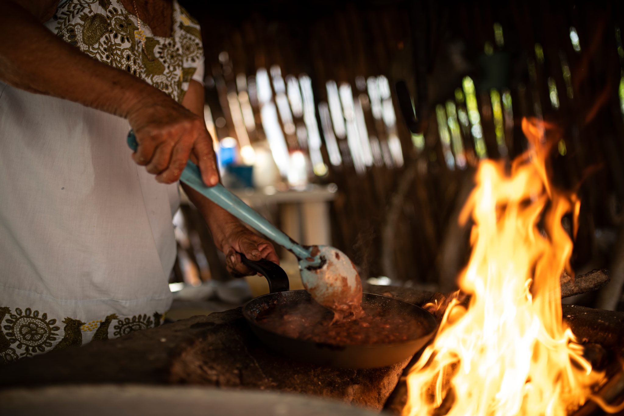 A woman stirs a pot over an open fire in the thatched kitchen.