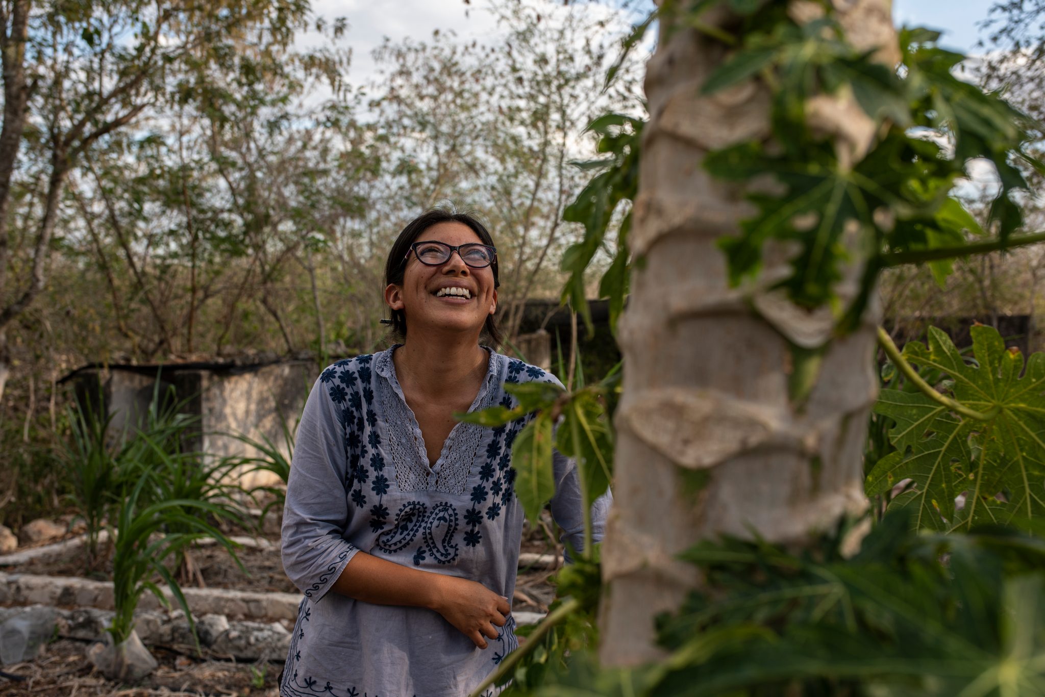Still laughing, she looks up past the palm trunk.
