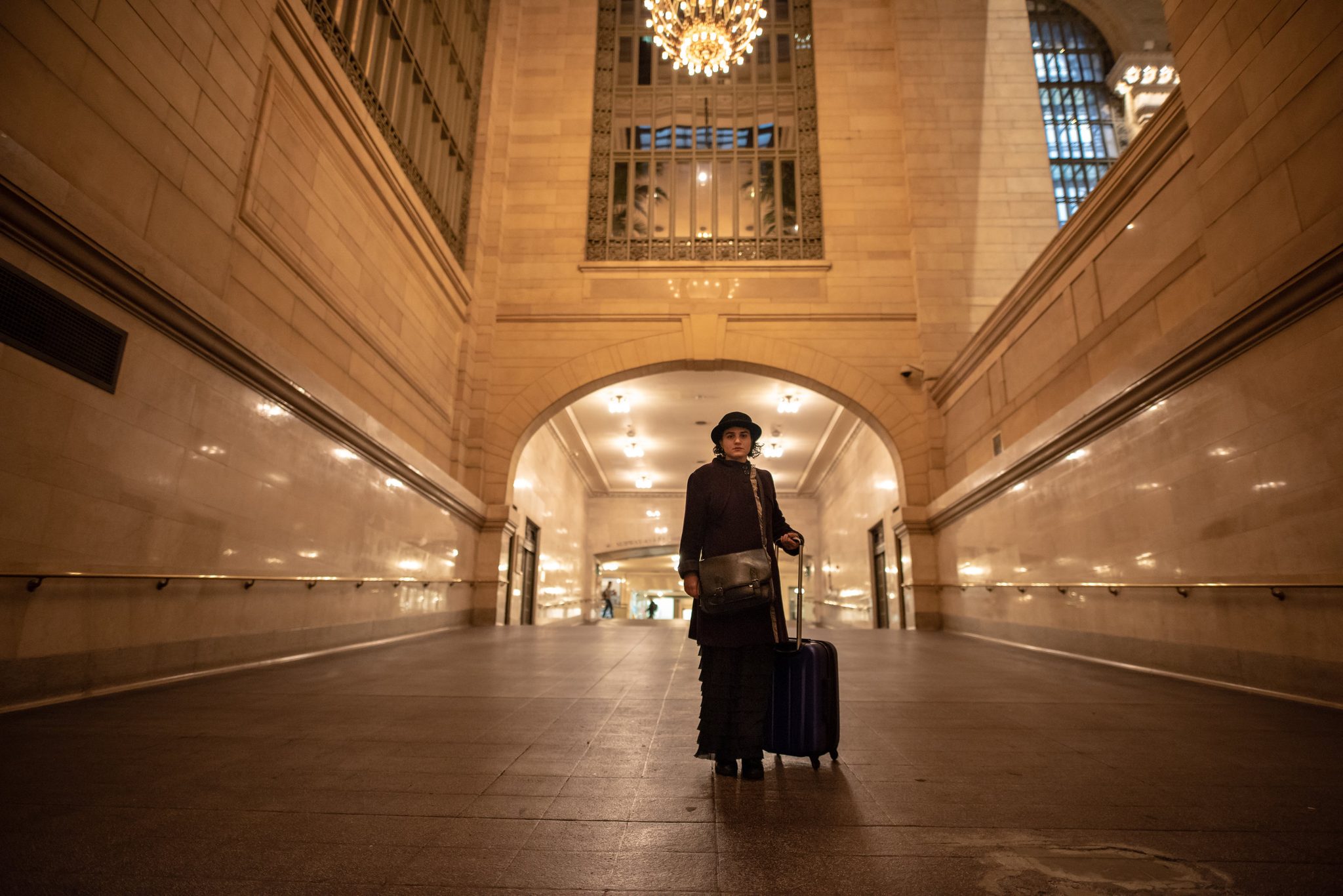 Samantha Echo arrives through the passage in her bowler hat, rolling her suitcase into Grand Central.
