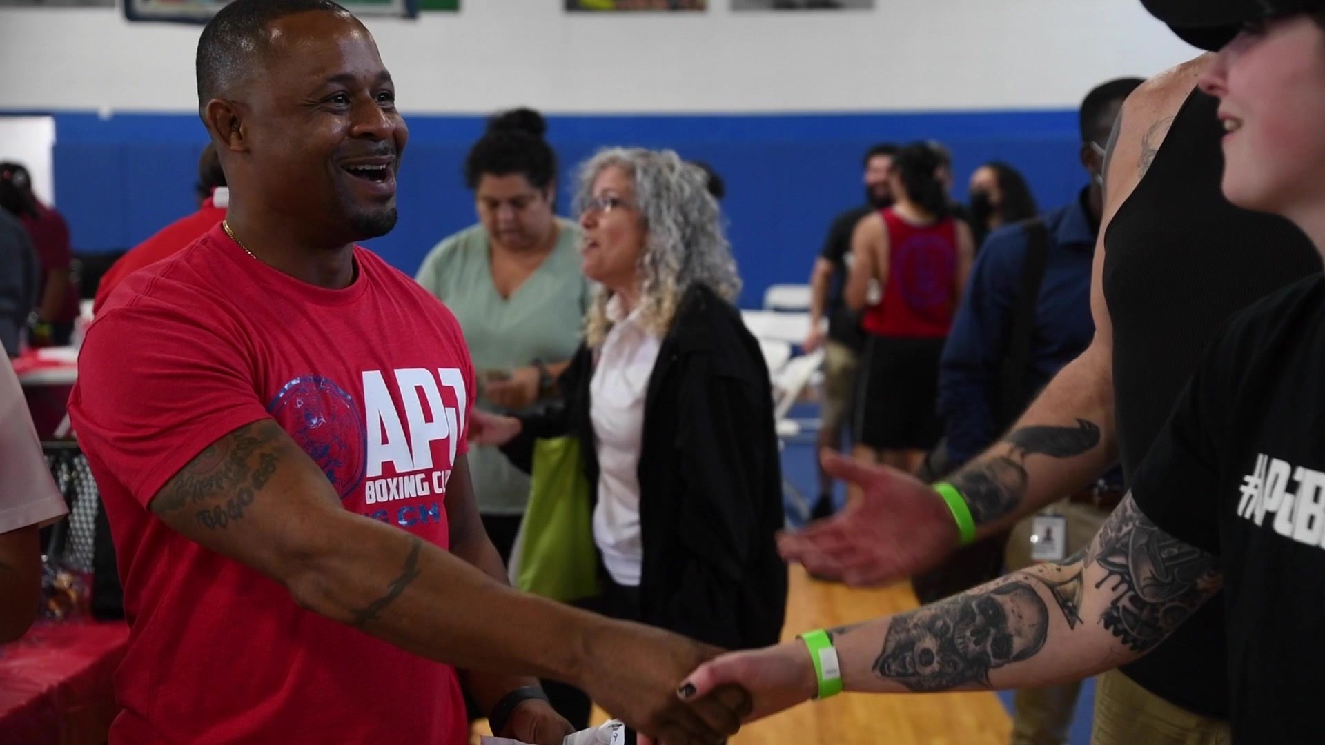 Coach Kariym breaks into a smile, shaking hands on the crowded gym floor at fight night.