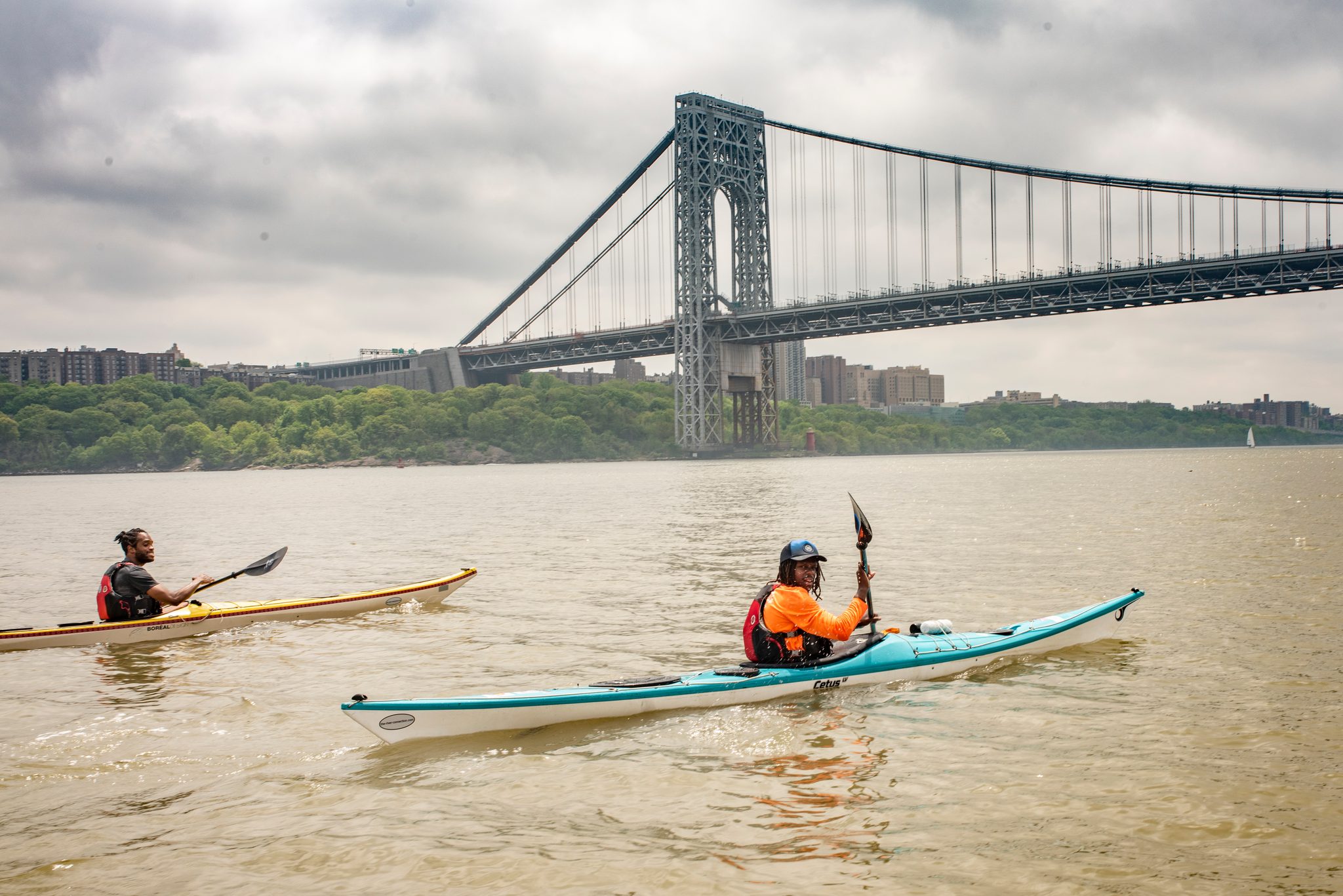 Two kayaks in brown spring water with the George Washington Bridge towering over the Manhattan shore.