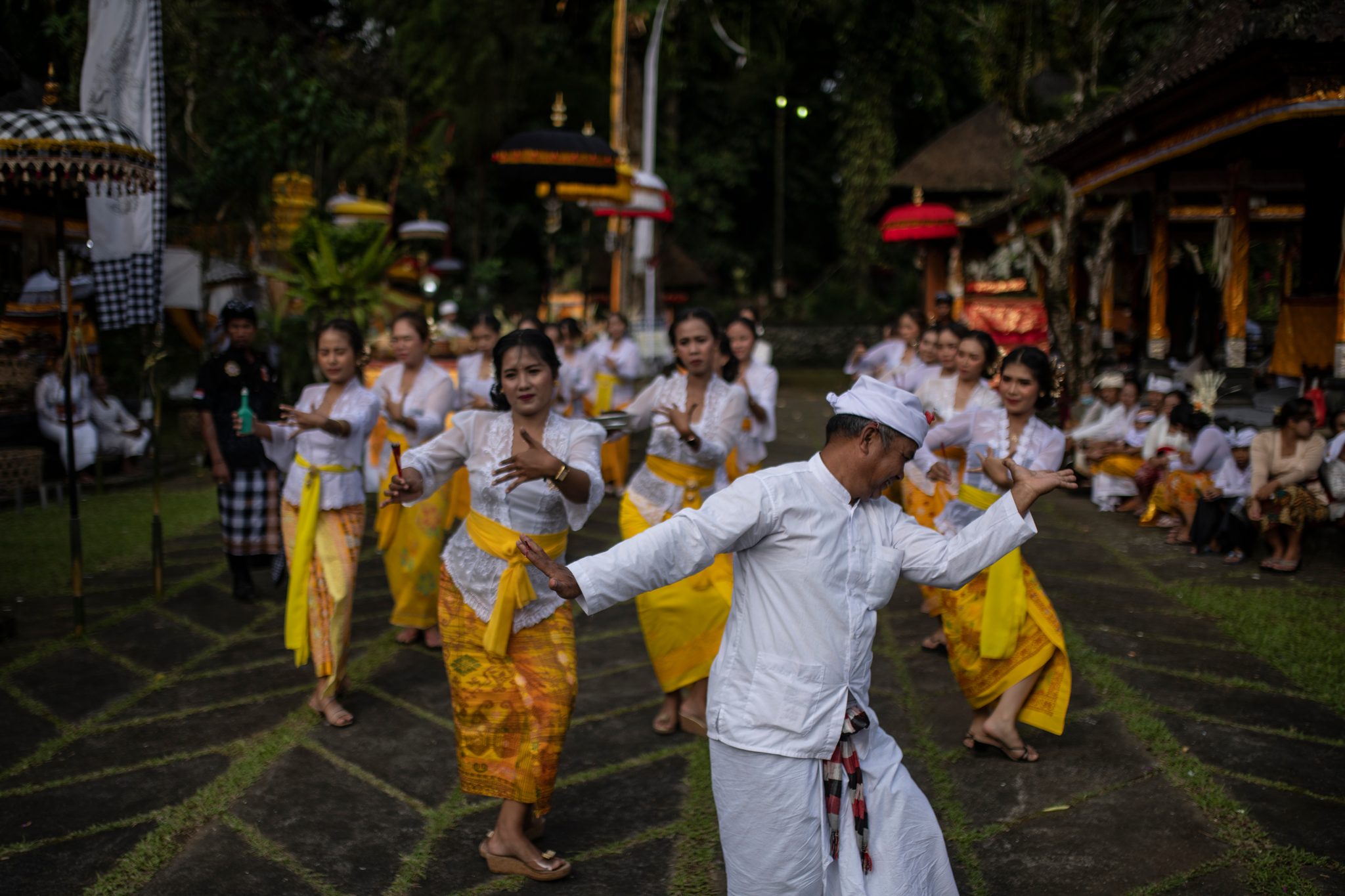 A man in white joins the dancing women, arms out, finding the same slow rhythm.