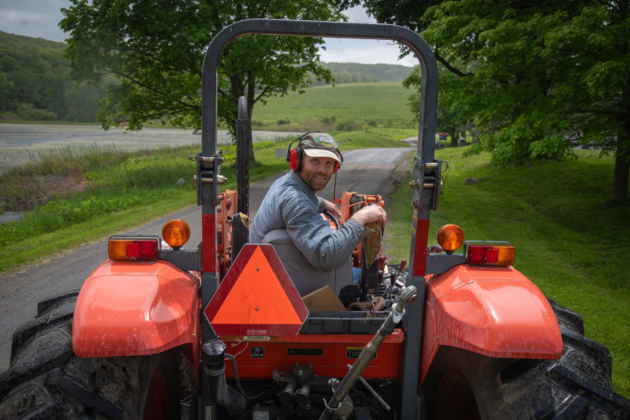 The tractor driver glances back on the lane beside the pond.