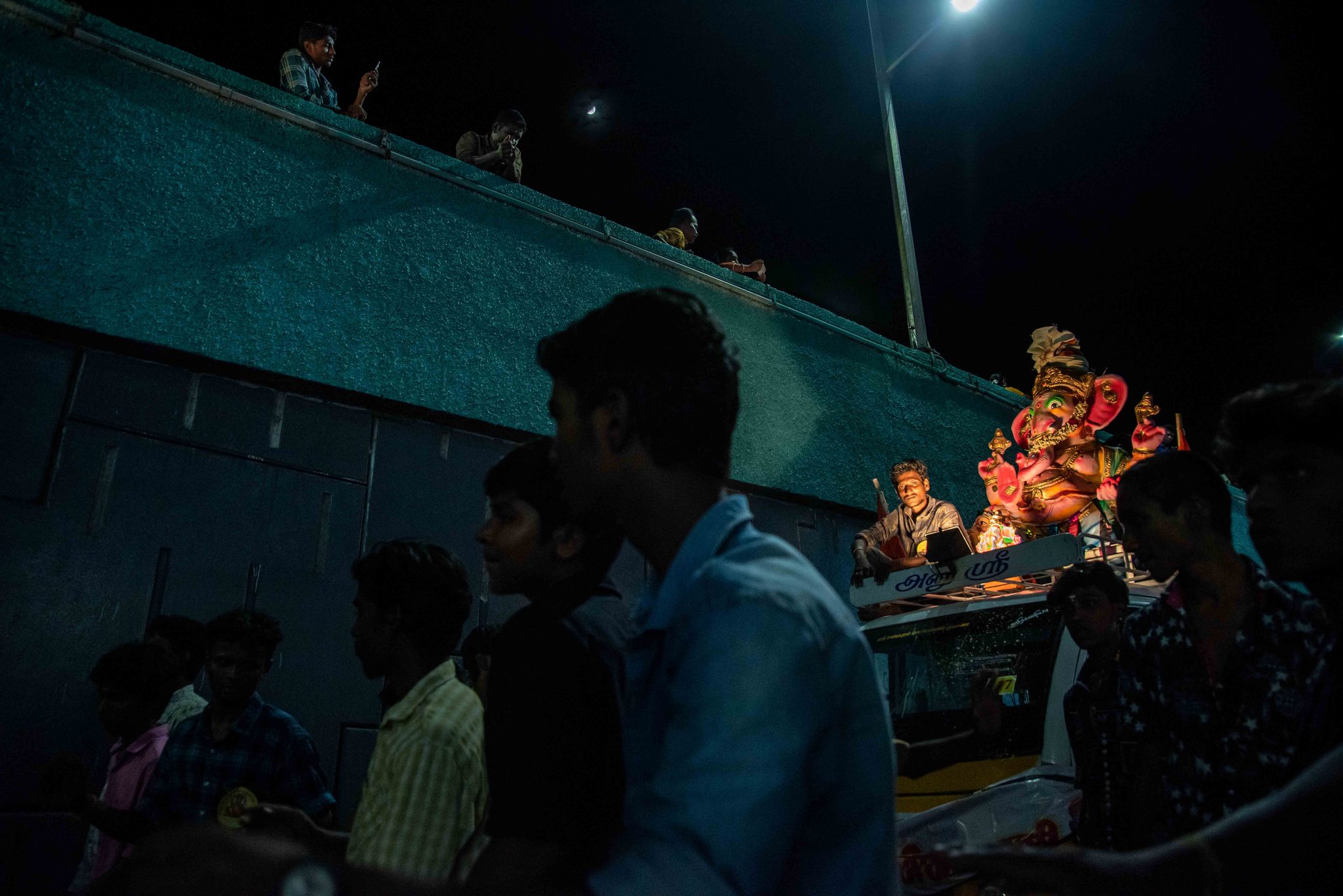 The crowd gathers at night as Ganesha rides past on a lit float.
