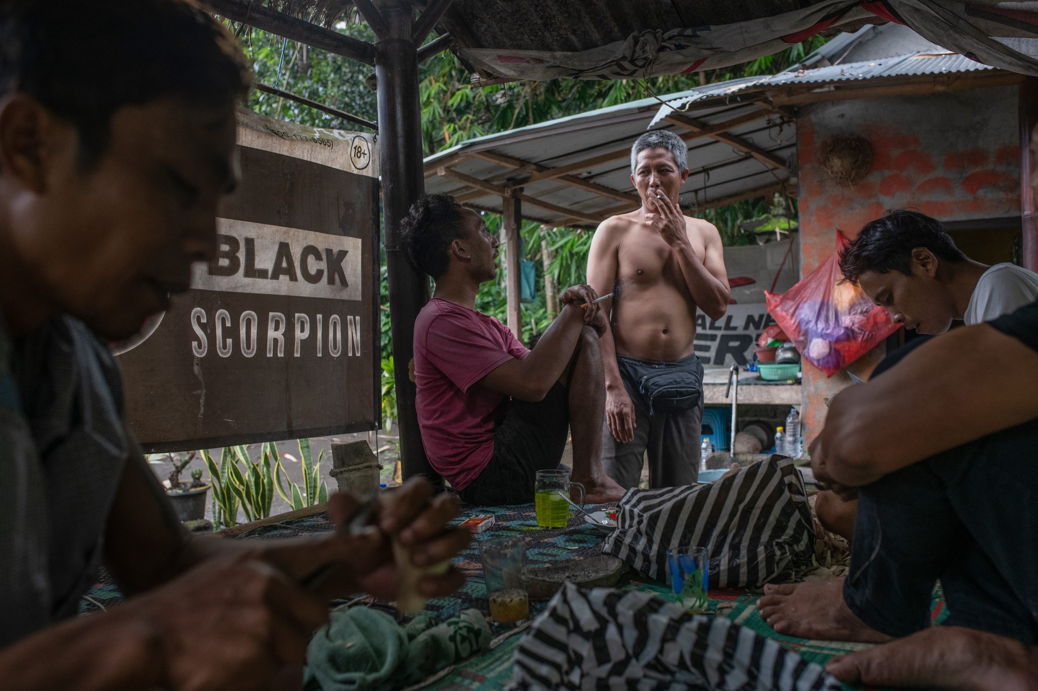 Men sit and carve on the mat beneath a sign that reads Black Scorpion.