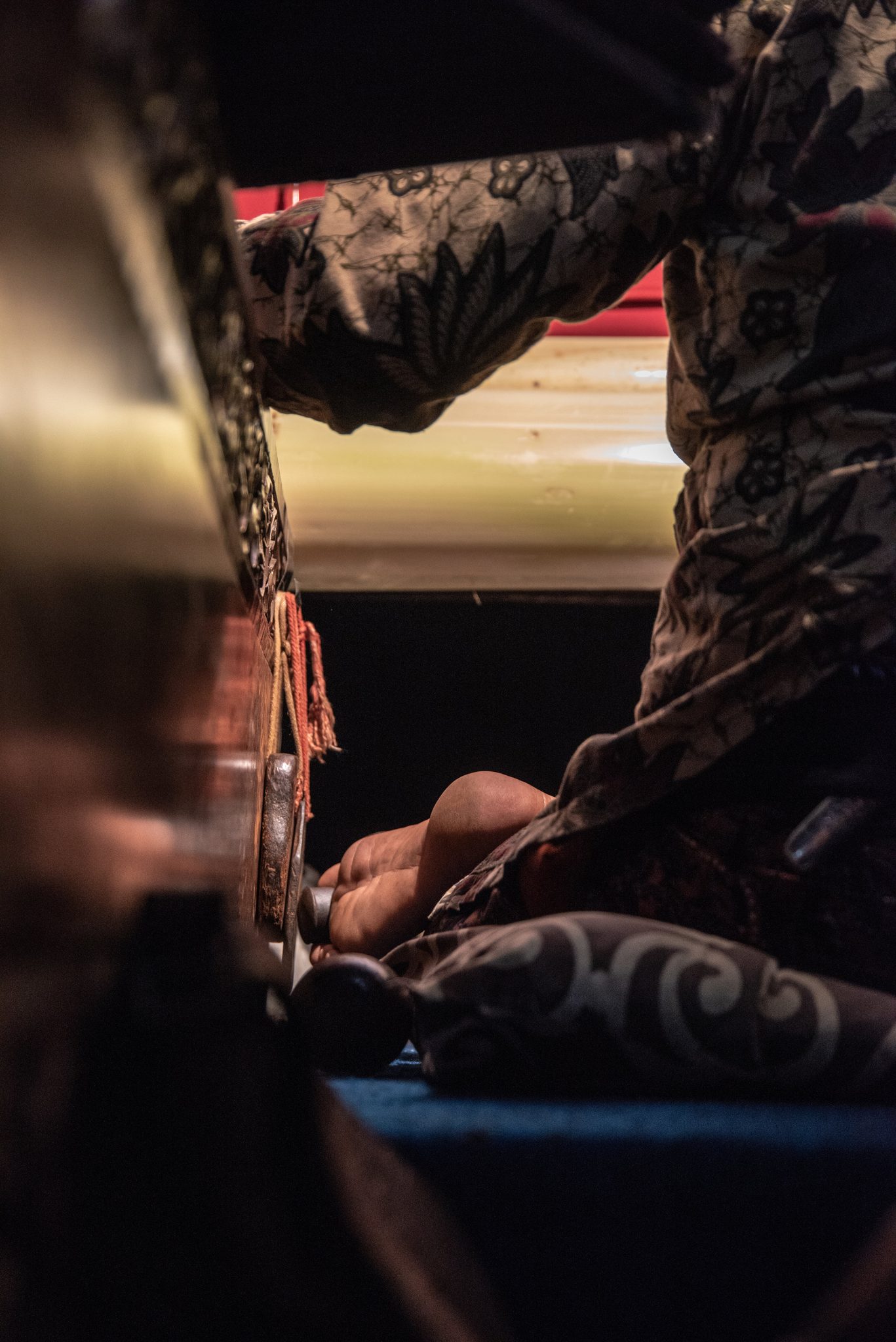 In the dark beside the stage, a bare foot keeps time against the hanging metal plates.