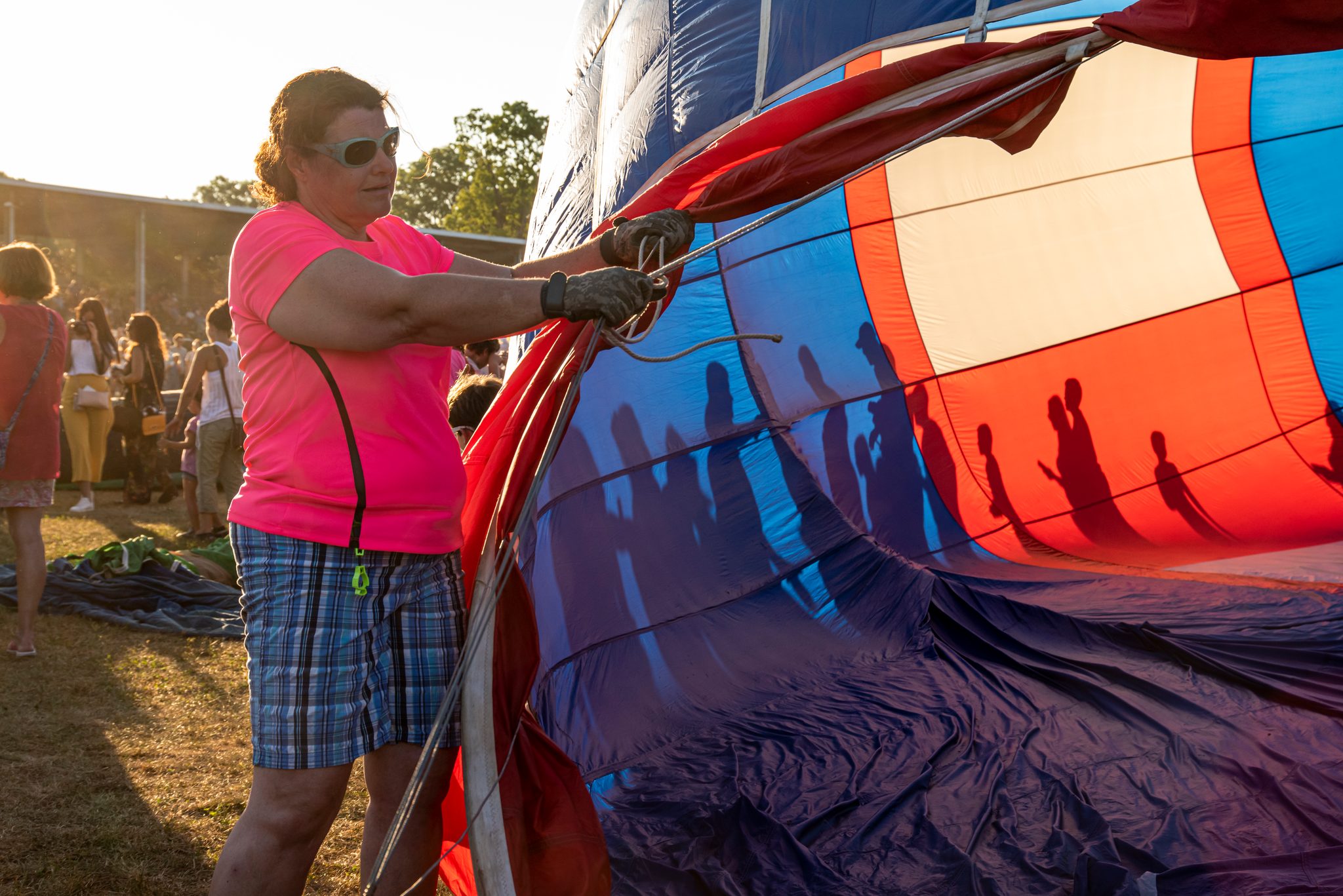 A woman steadies the envelope while the crowd's shadows fall across the fabric.