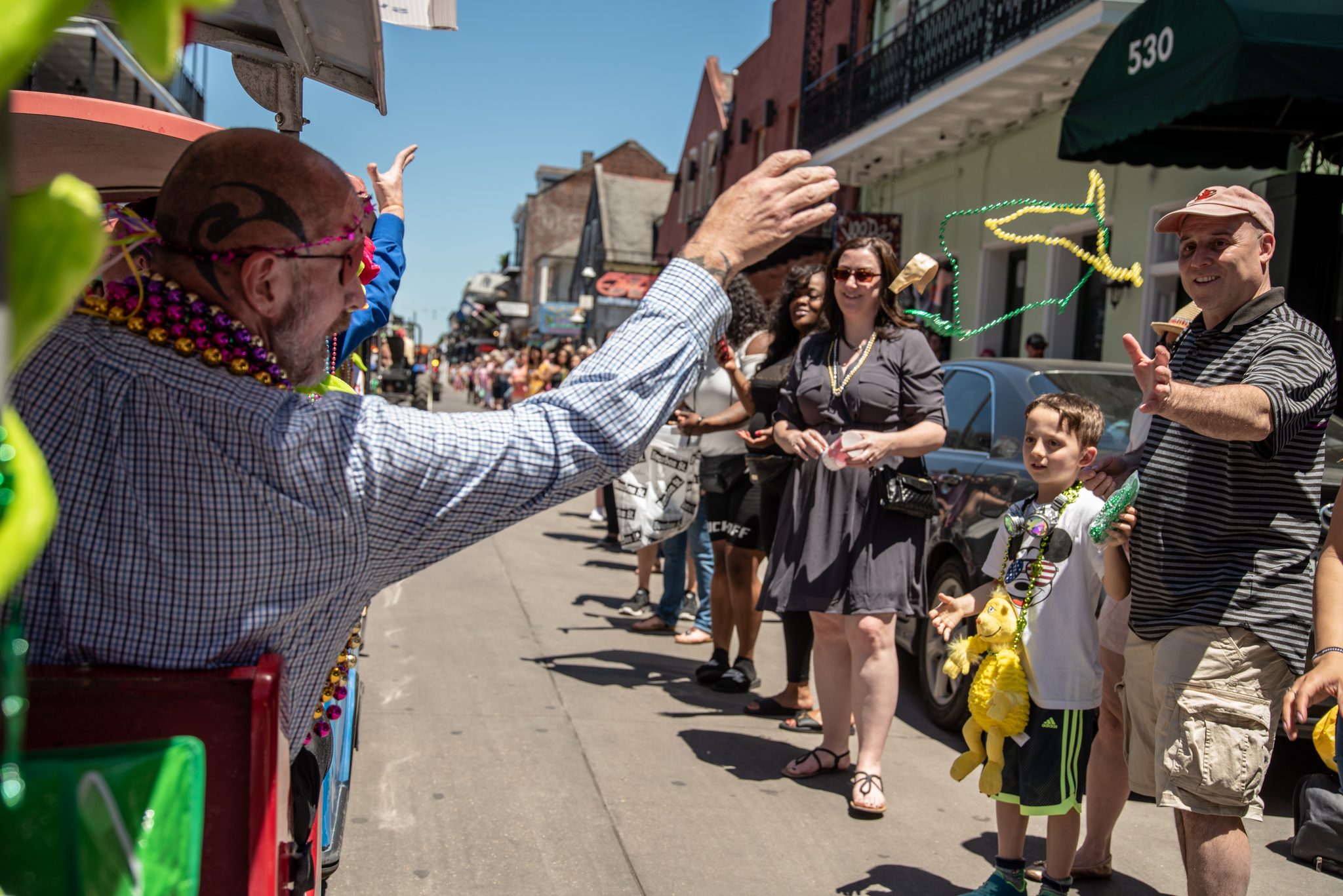 A rider leans from his float toward the sidewalk, where every hand is up and every neck is heavy with beads.
