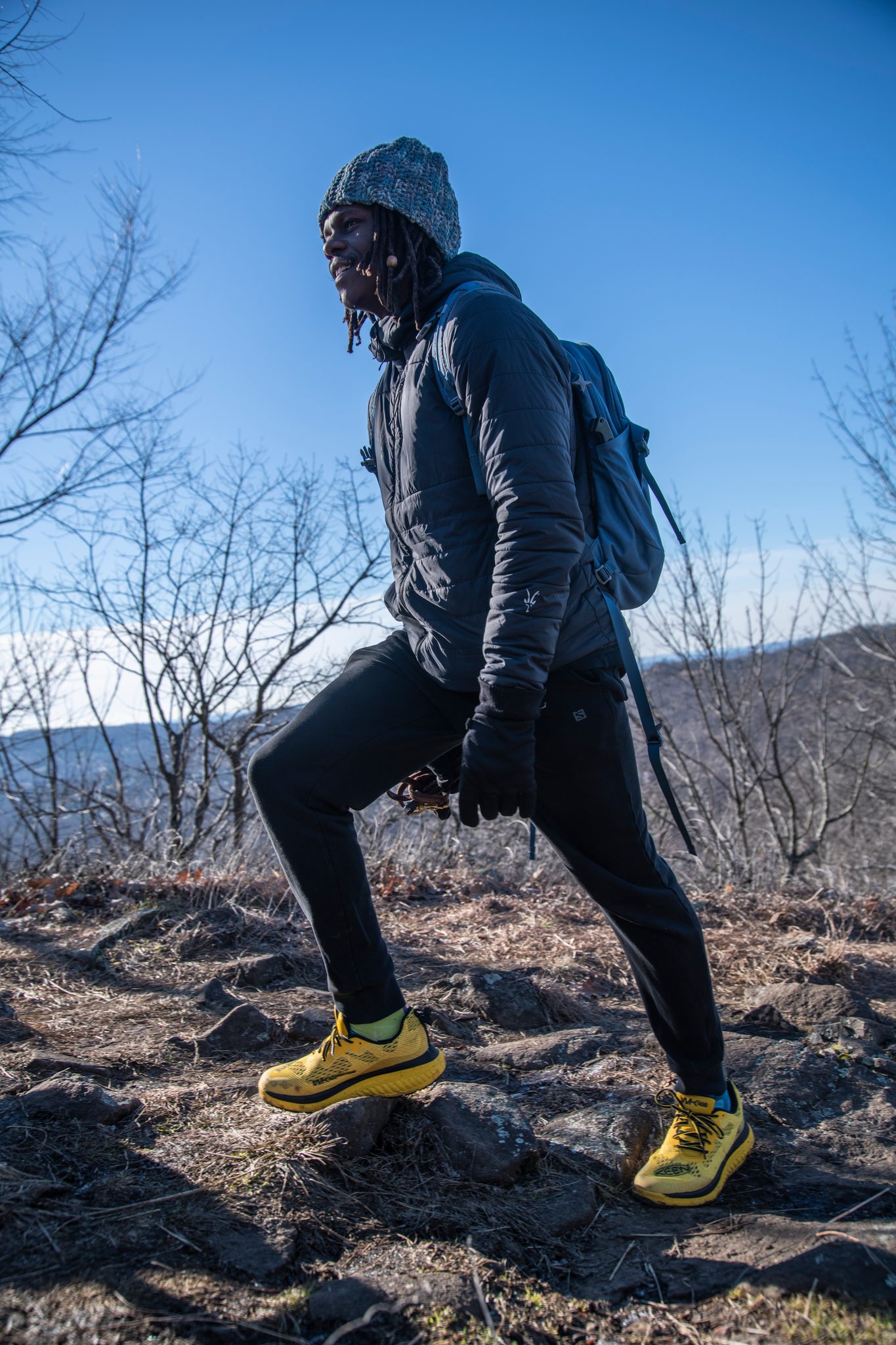 Chev climbs the last stretch of open rock toward the ridge, distant hills pale behind him.