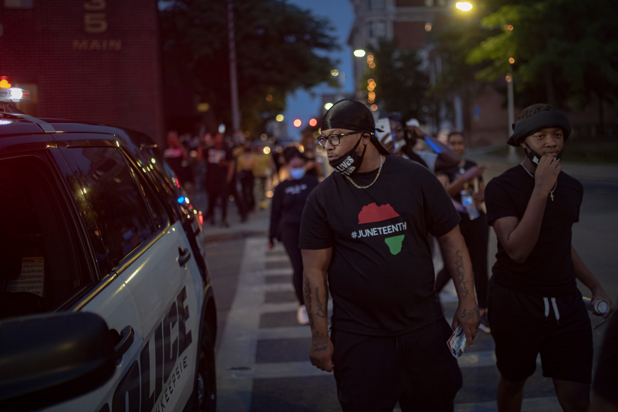 A marcher in a Juneteenth shirt walks past a police SUV, and the whole street follows.