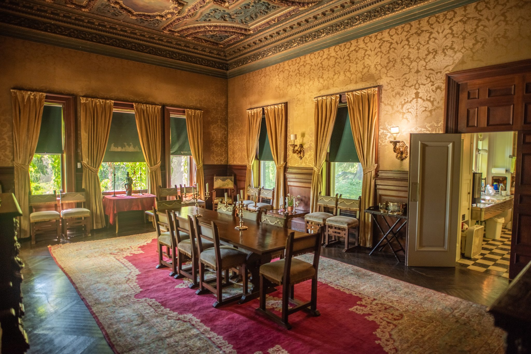 The bungalow dining room, gold damask and an ornate painted ceiling above a long oak table and a red carpet.