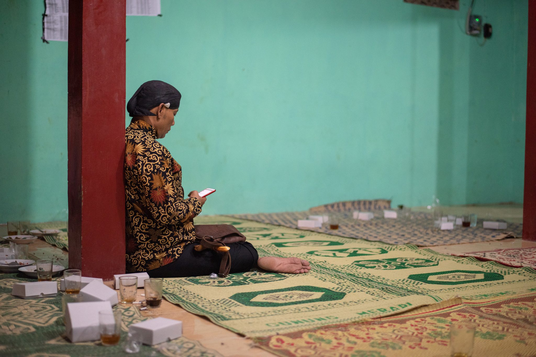 Between the mats and the empty glasses, a man checks his phone against the pillar.