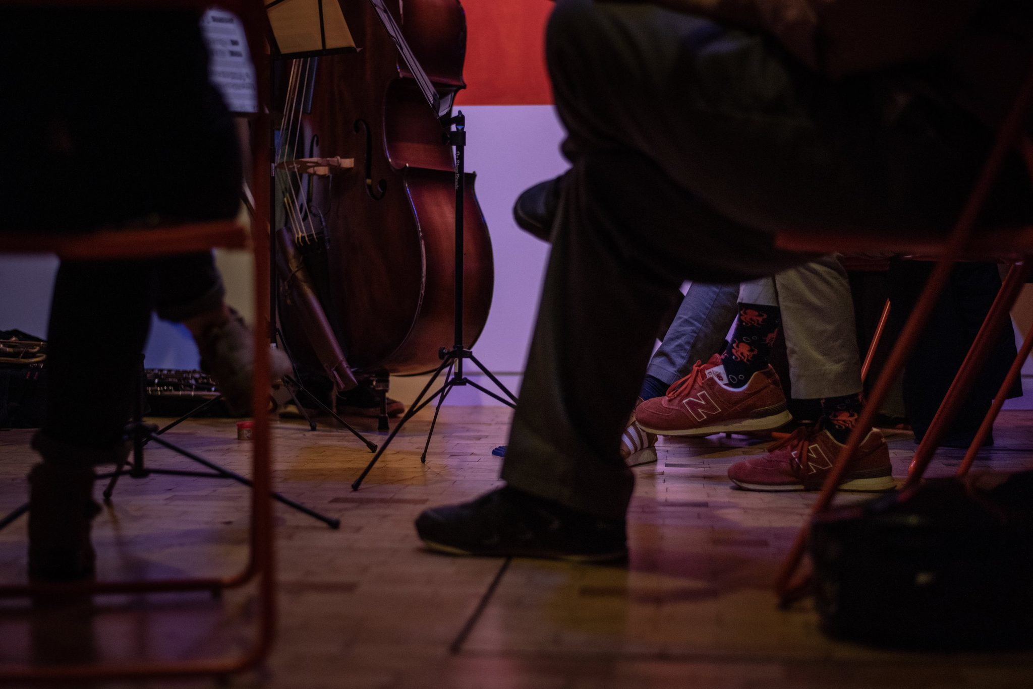 Under the chairs, a pair of red sneakers, a bass and a forest of music stands.