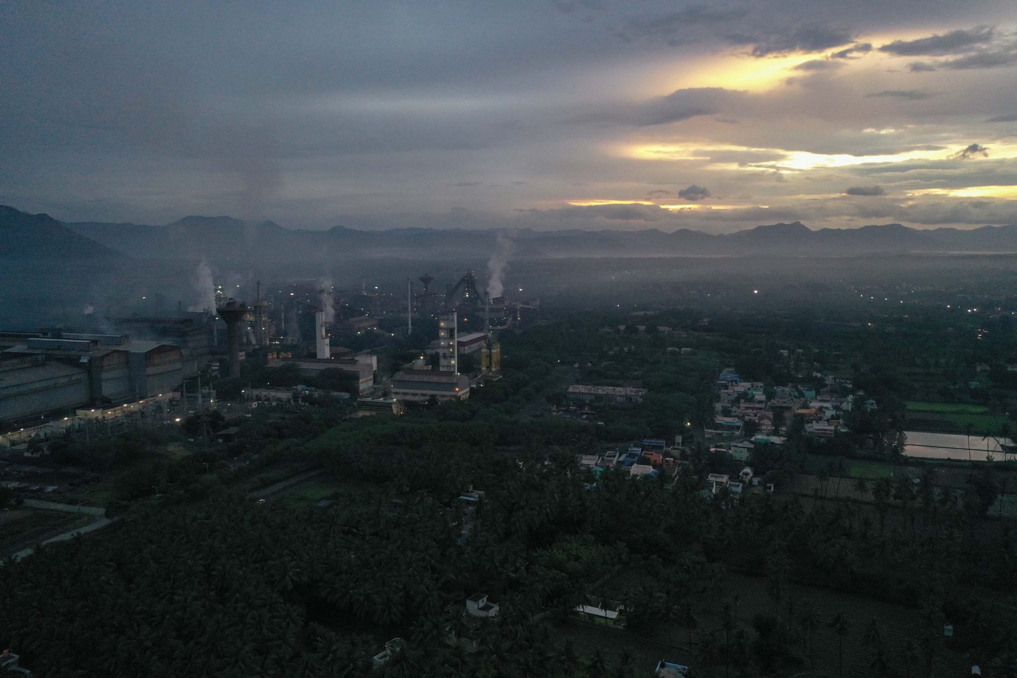 Steam drifts from the factory while the town wakes beneath low clouds.