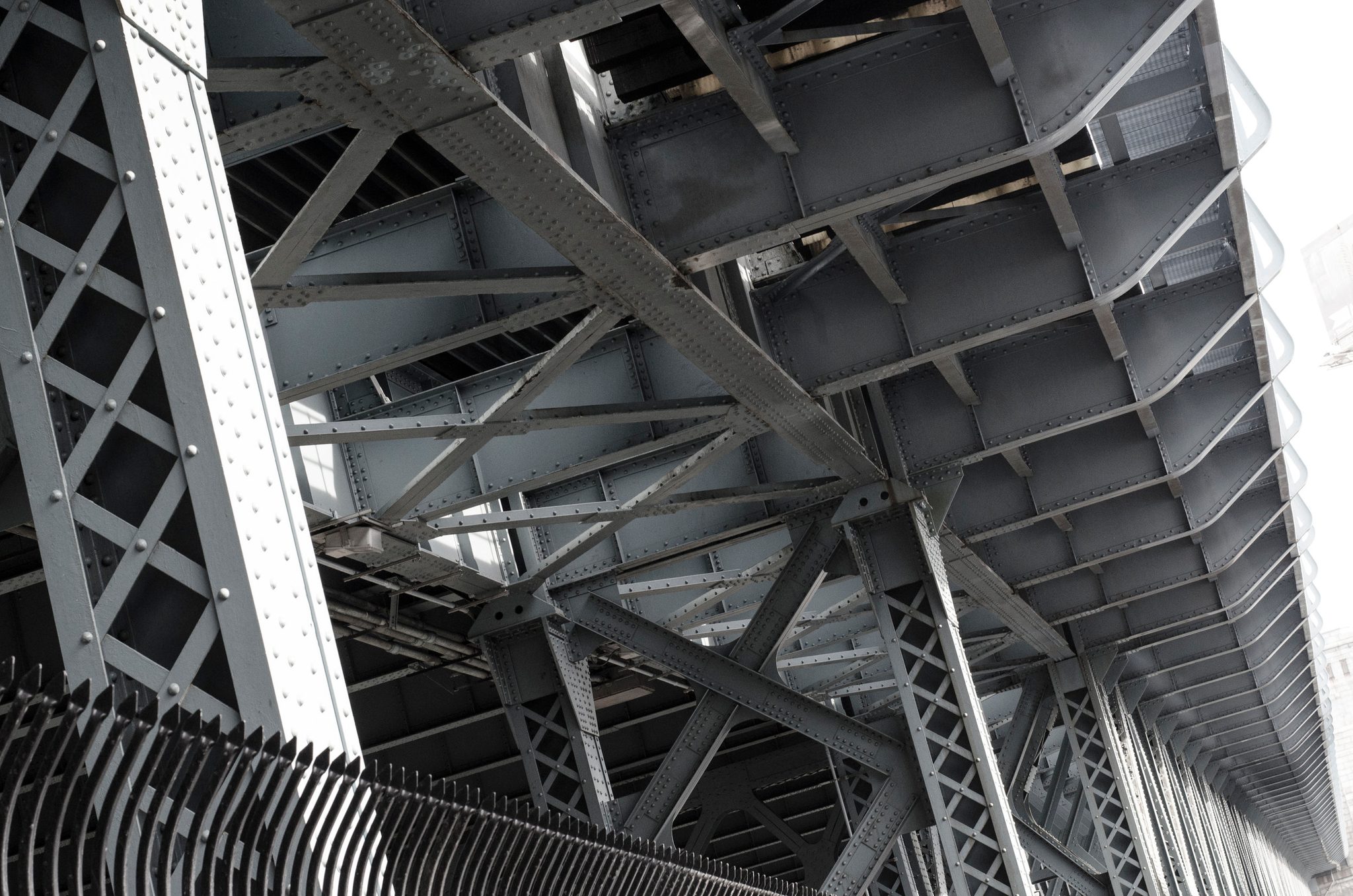 Steel beams and rivets crisscross beneath a bridge.
