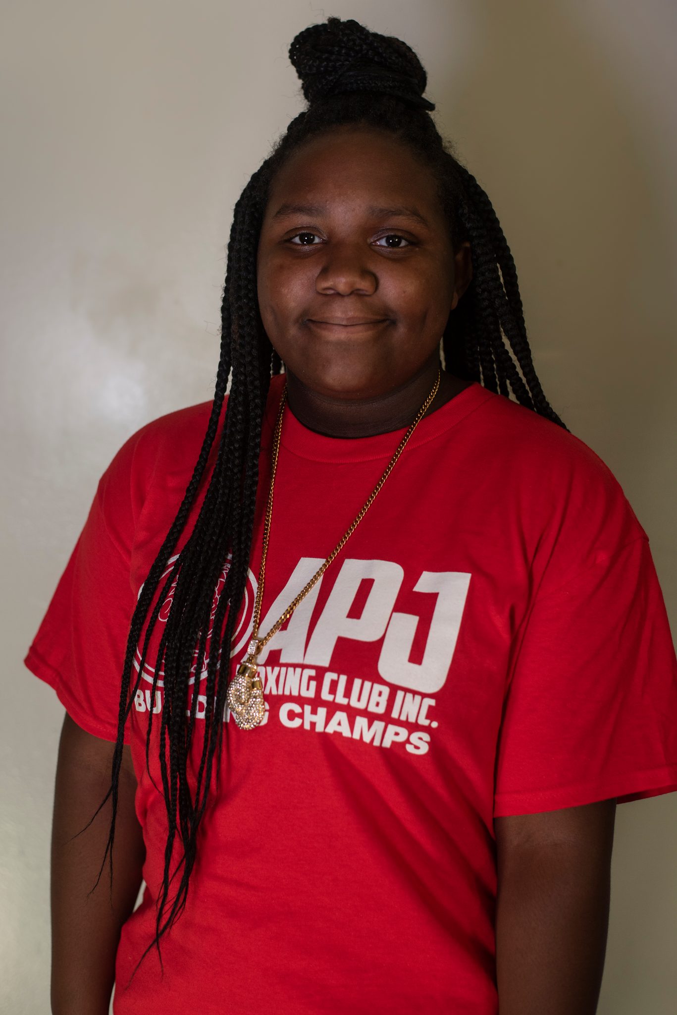 Braids down to her waist and a gold chain over the club shirt, she gives the lens a soft smile.