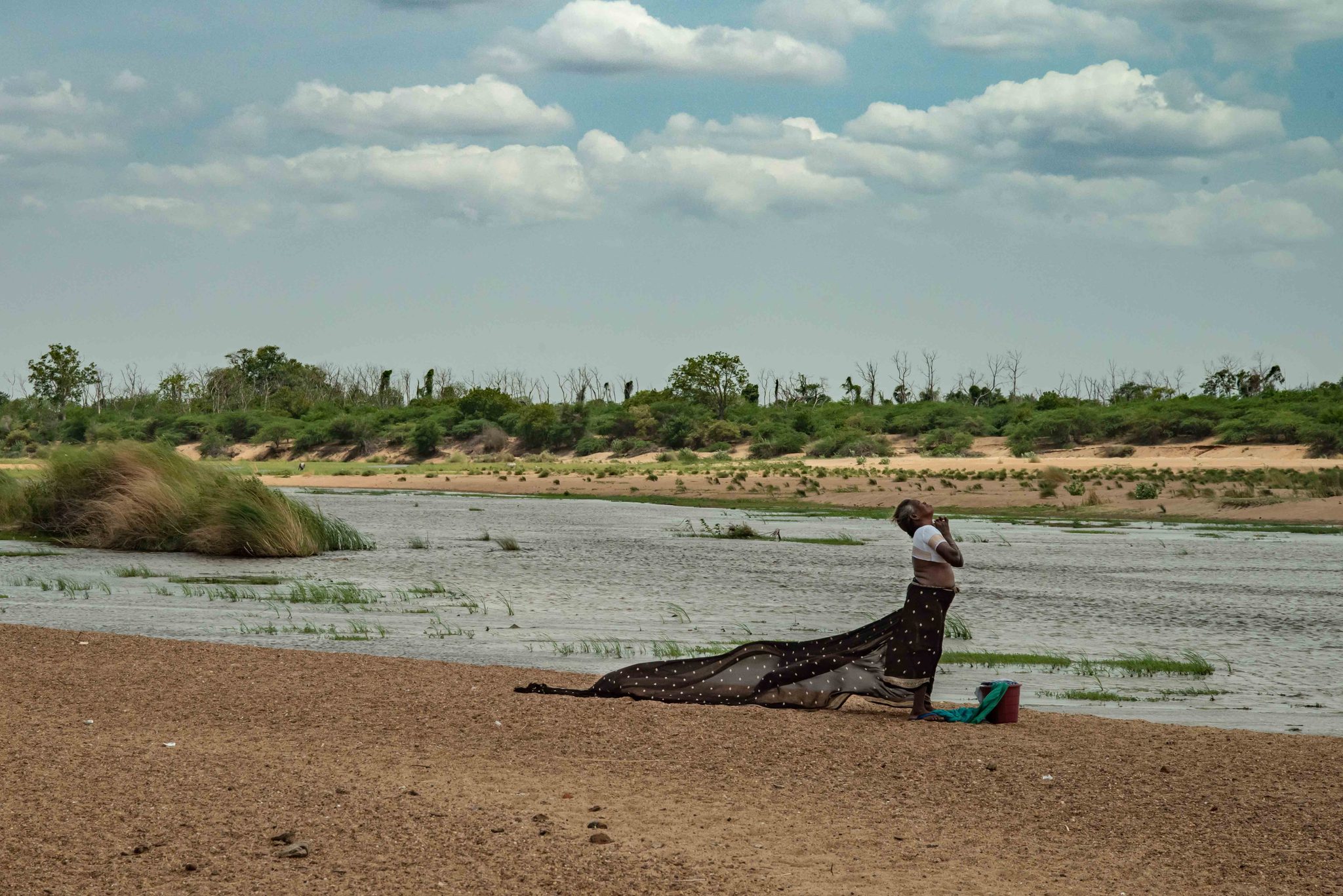 A woman spreads a long cloth to dry on the riverbank.