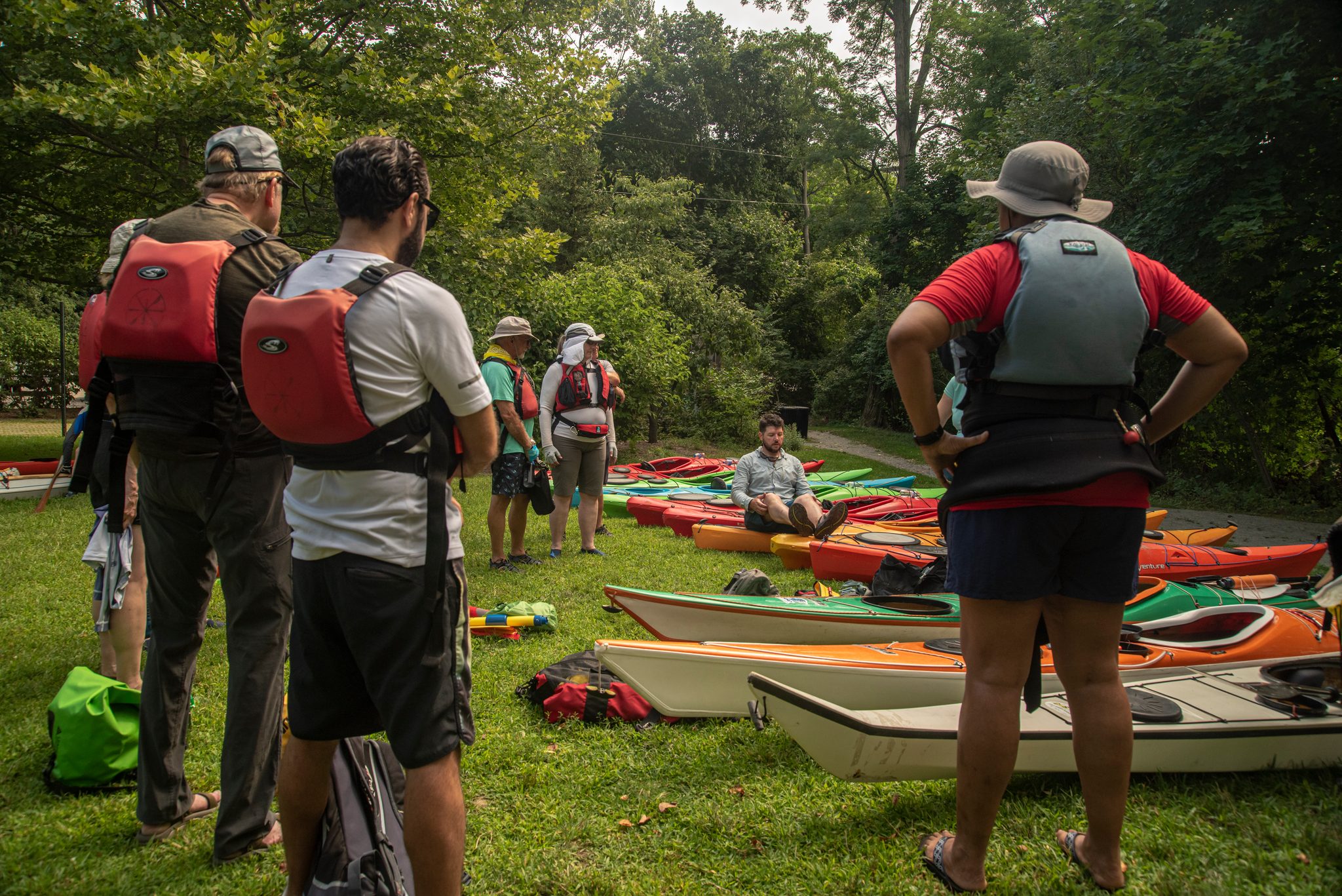 Life vests on, the group listens before putting in, a rainbow of kayaks waiting on the grass.