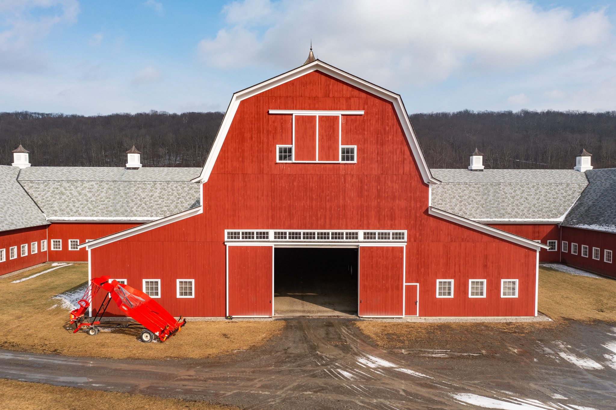 A red gambrel barn with white trim stands broadside to the camera on a bare late February afternoon.