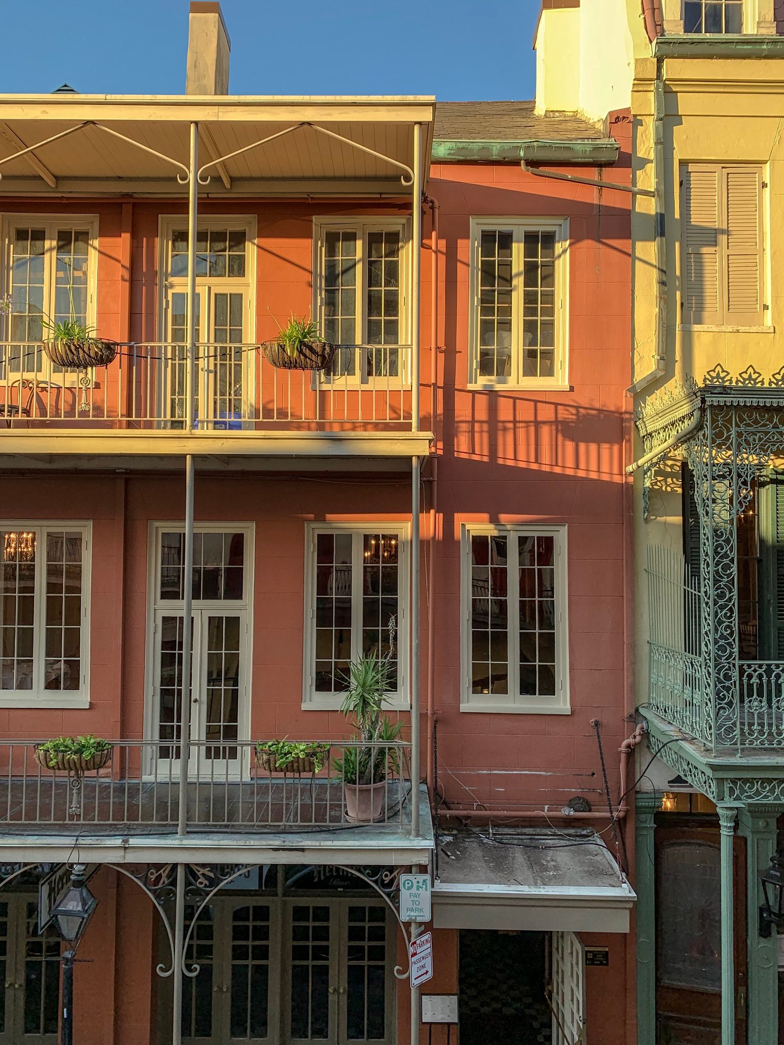 Iron balconies and potted plants line a French Quarter facade in coral and gold.