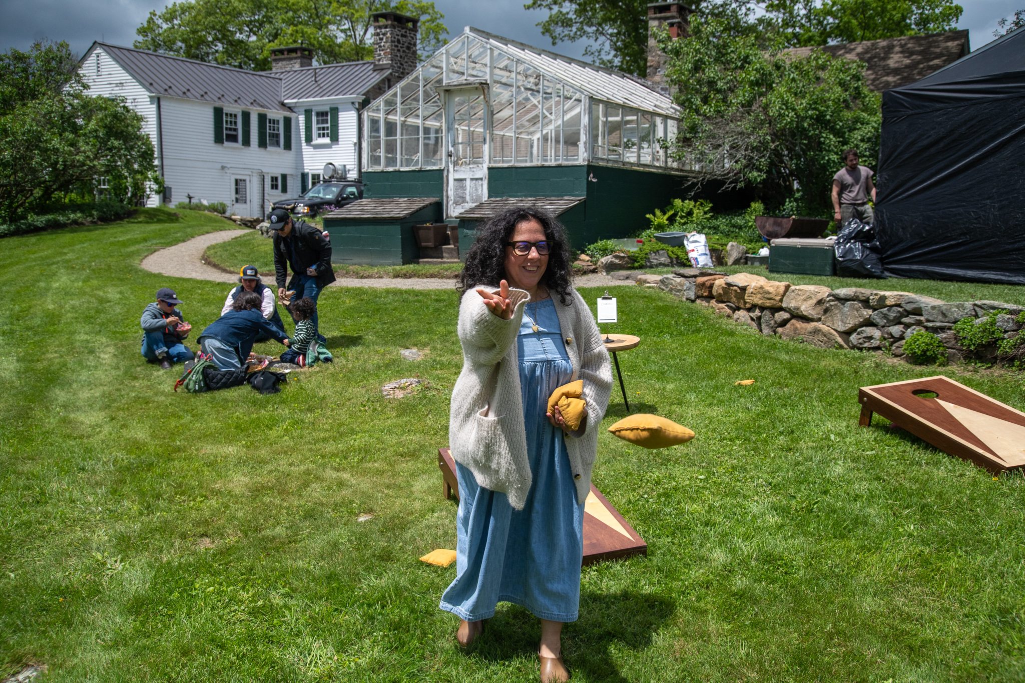 A woman lines up her cornhole toss on the lawn below the greenhouse.