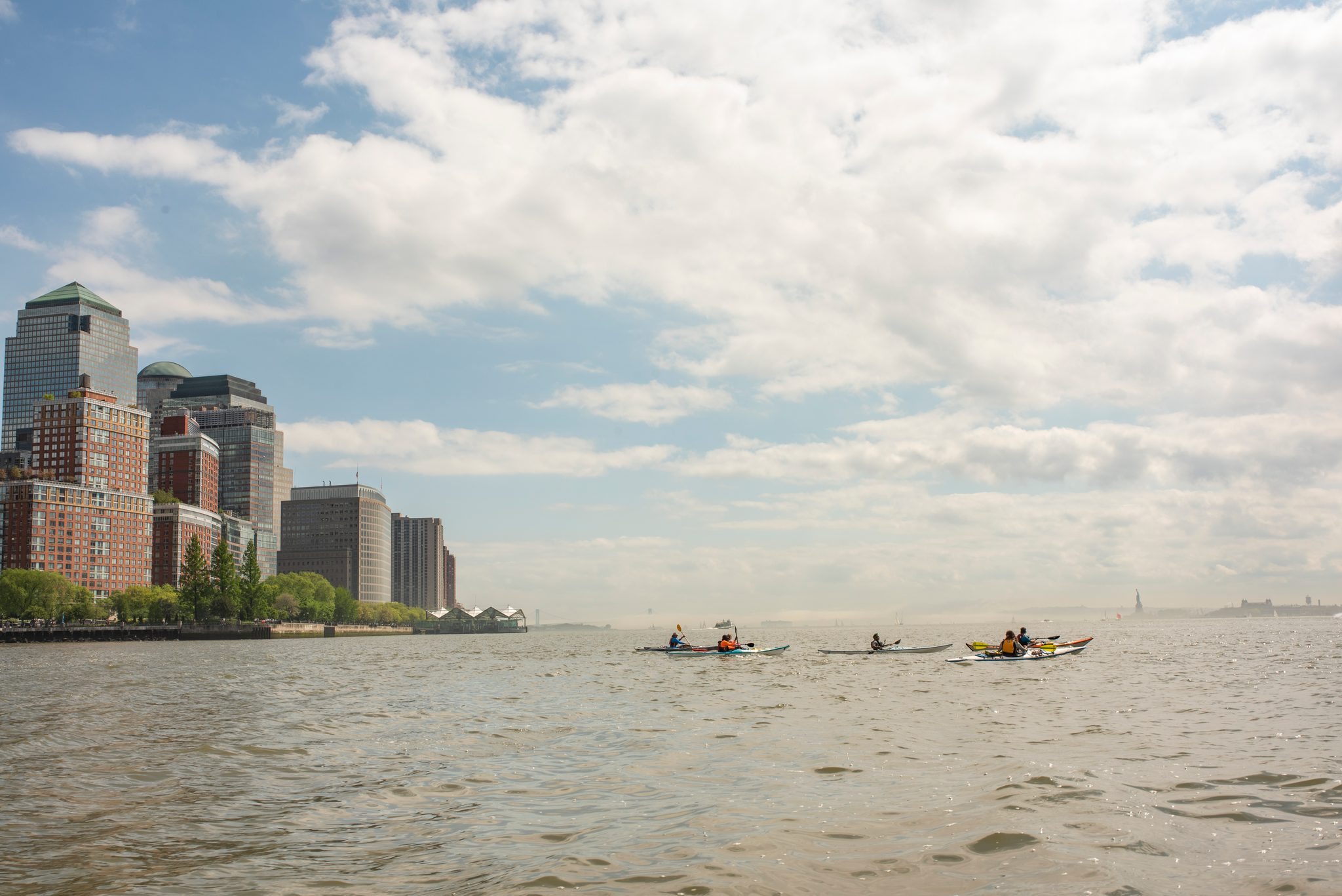 Three kayaks small against the harbor, the towers of lower Manhattan catching the afternoon sun.