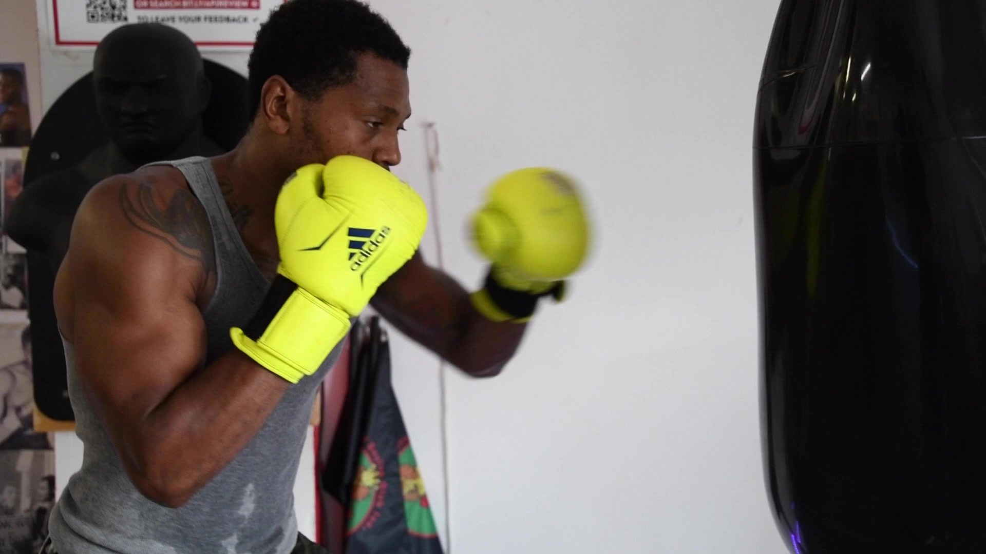 Neon gloves blur toward the heavy bag in the back corner, the only bright color against white walls.