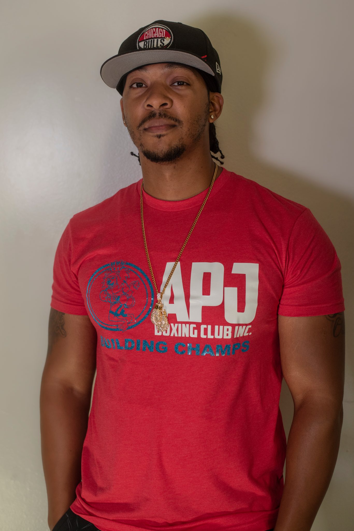 In a Bulls cap and a gold chain, he stands easy with his arms loose at his sides.