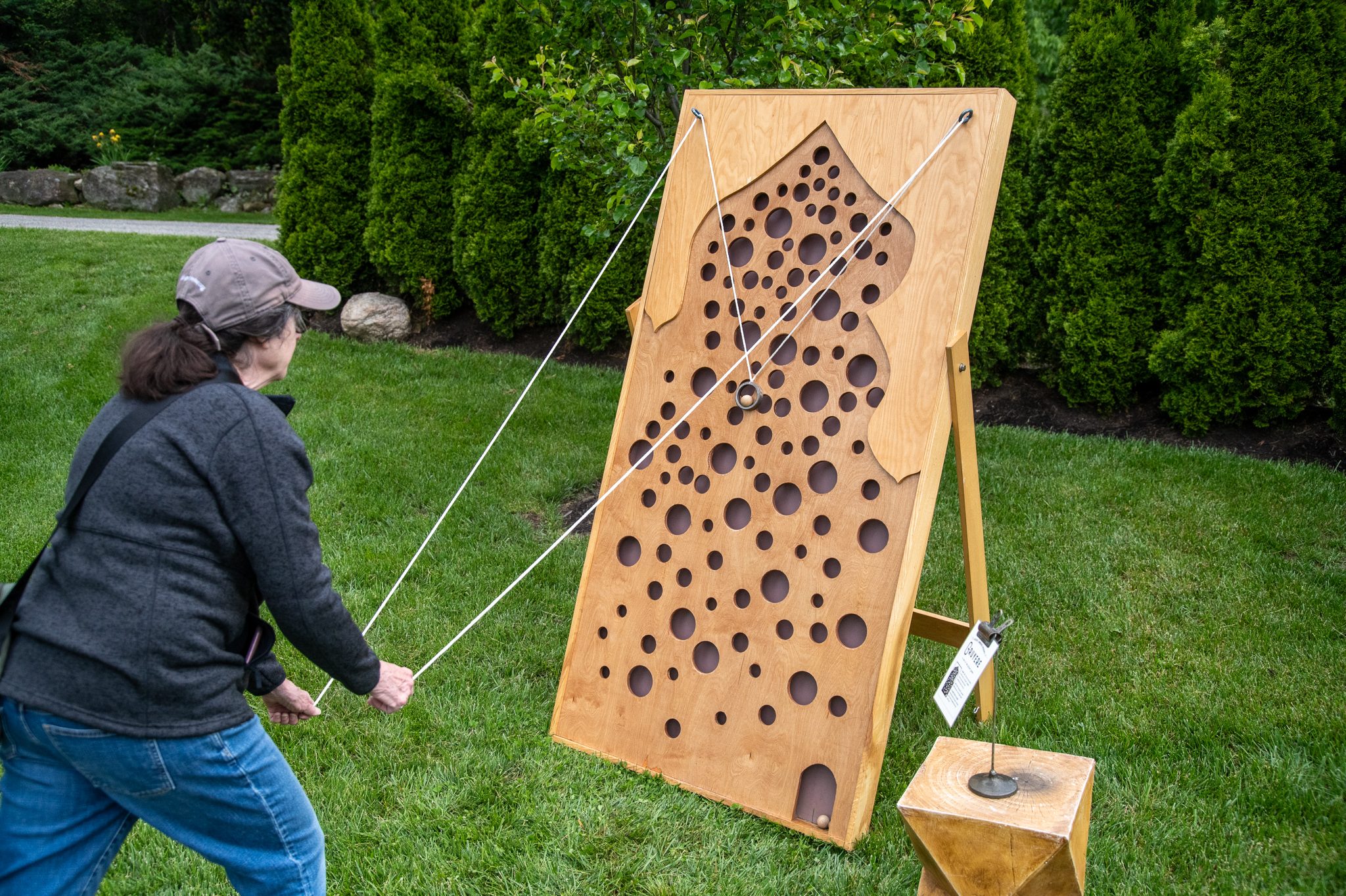 A visitor works the strings of a handmade wooden ball game on the lawn.
