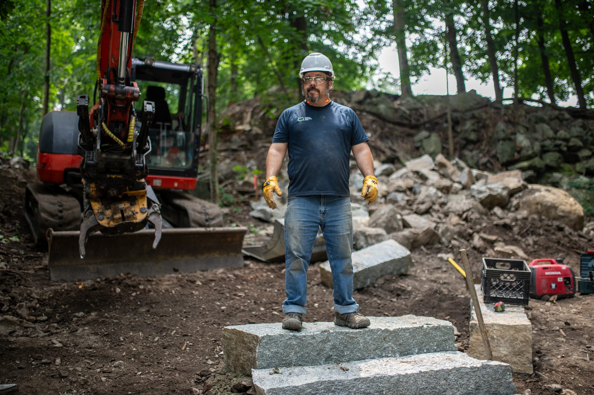 He stands at the top of the finished steps, the excavator behind him.