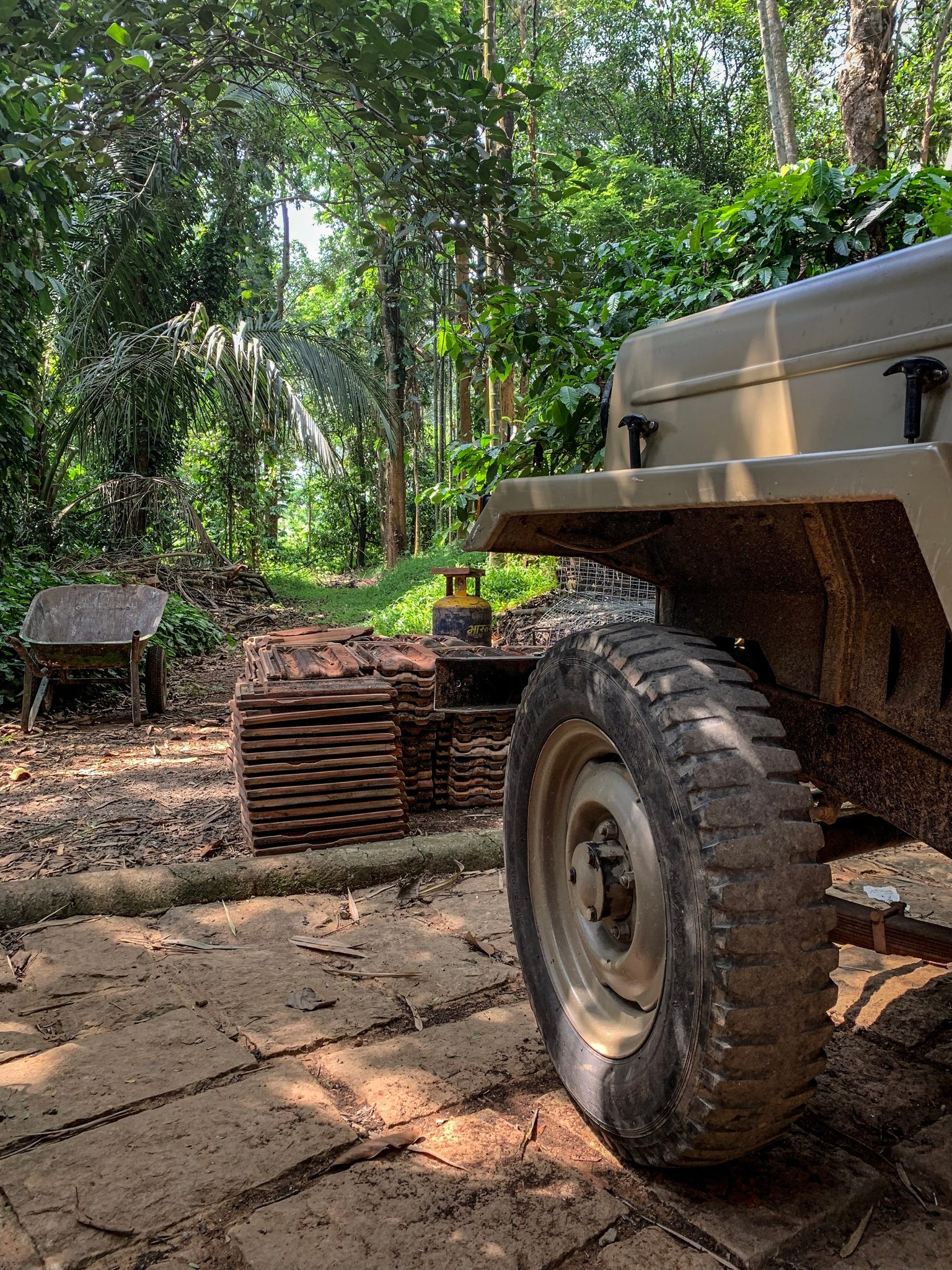 An old jeep rests in the clearing beside stacks of clay roof tiles, the forest pressing in.
