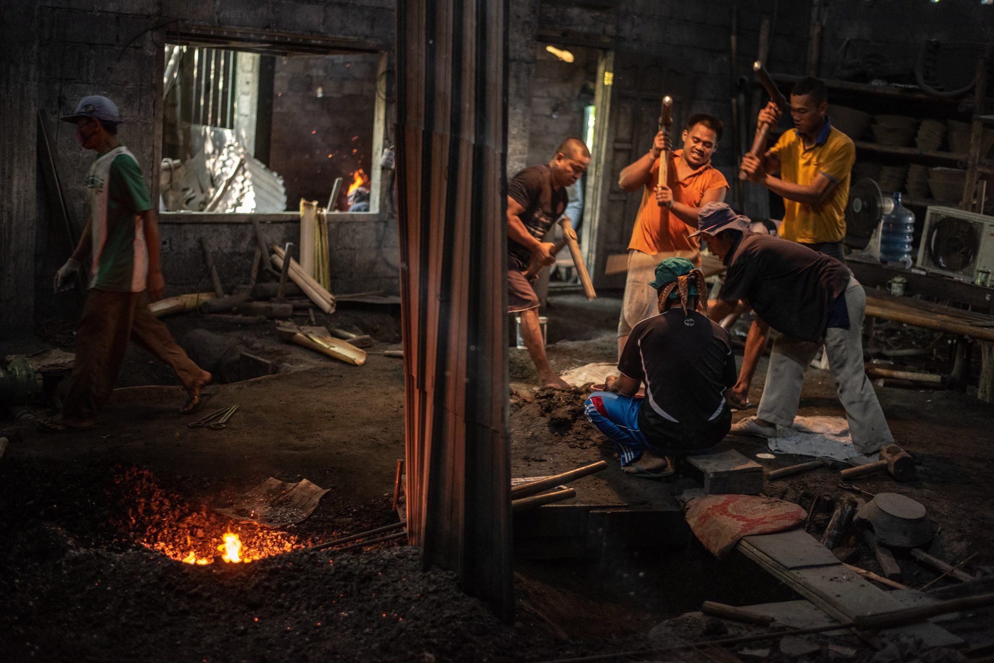A team of blacksmiths raises their hammers in turn while one man holds the hot metal steady.