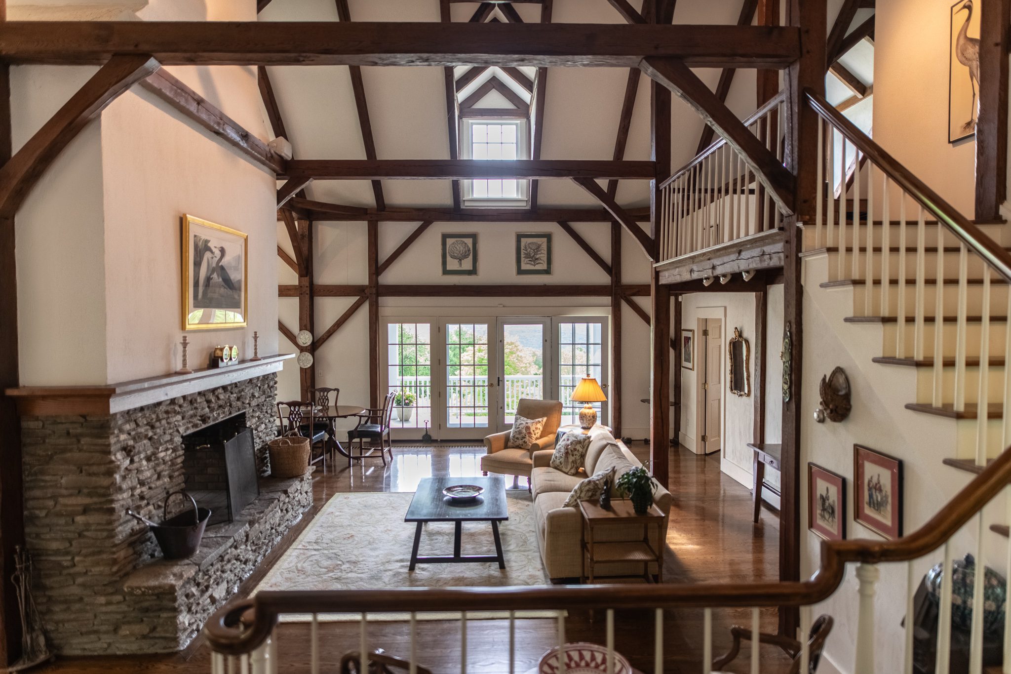 Timber framing climbs two stories over a fieldstone hearth, and late May afternoon light slips through the gallery windows.