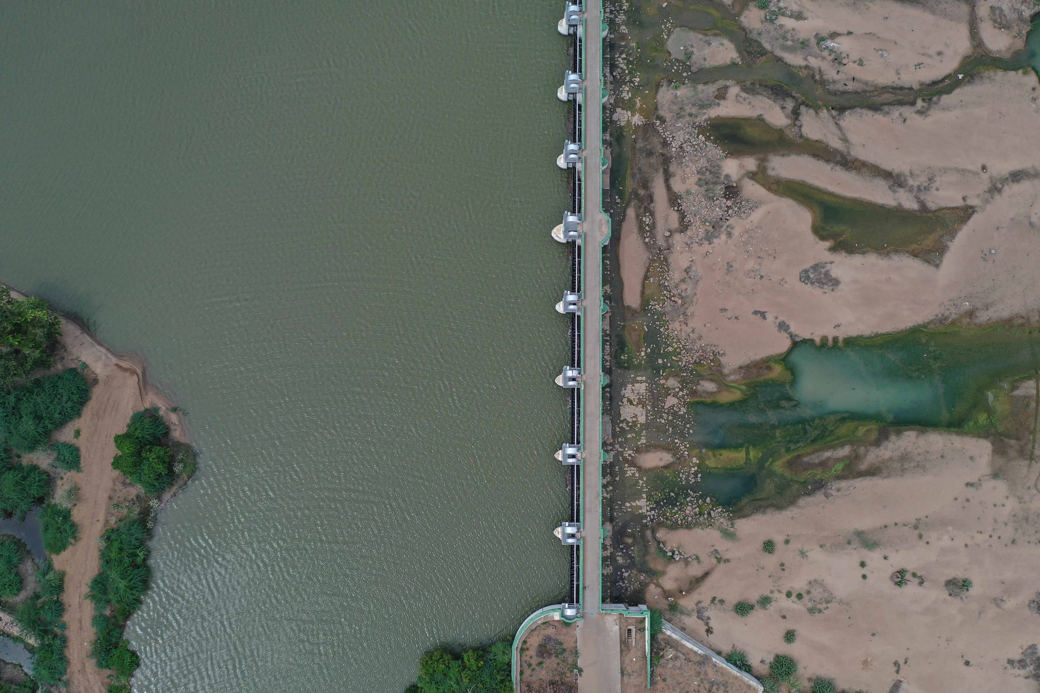 A barrage cuts across the frame, deep water on one side and sand on the other.