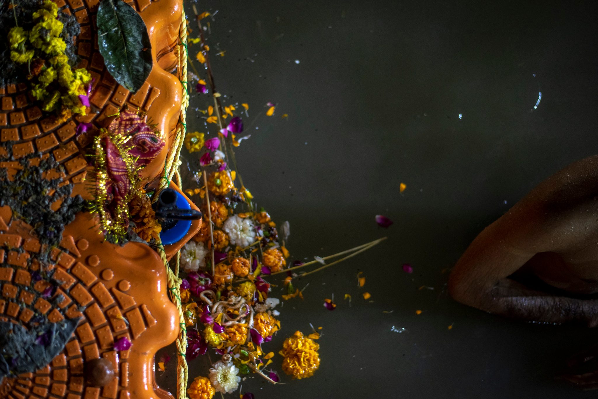 Petals and marigold garlands spill into the black water beside an orange float.